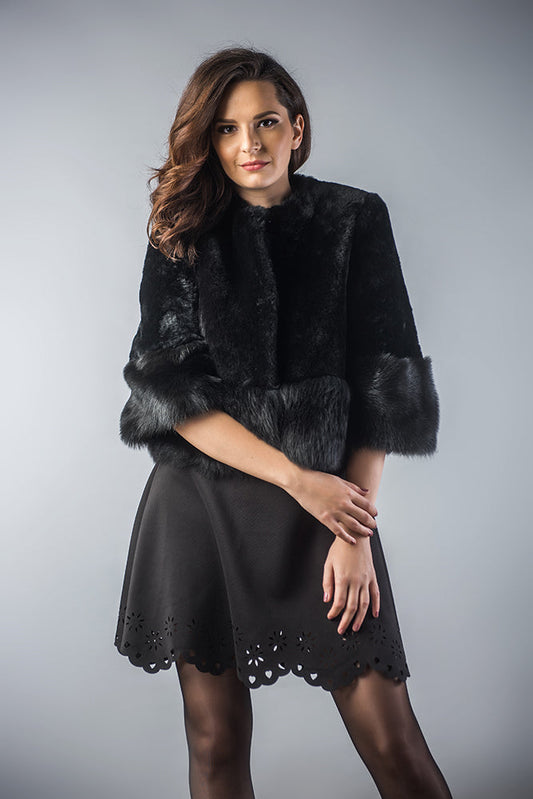 Woman wearing a black fur coat over a black dress on a gray background