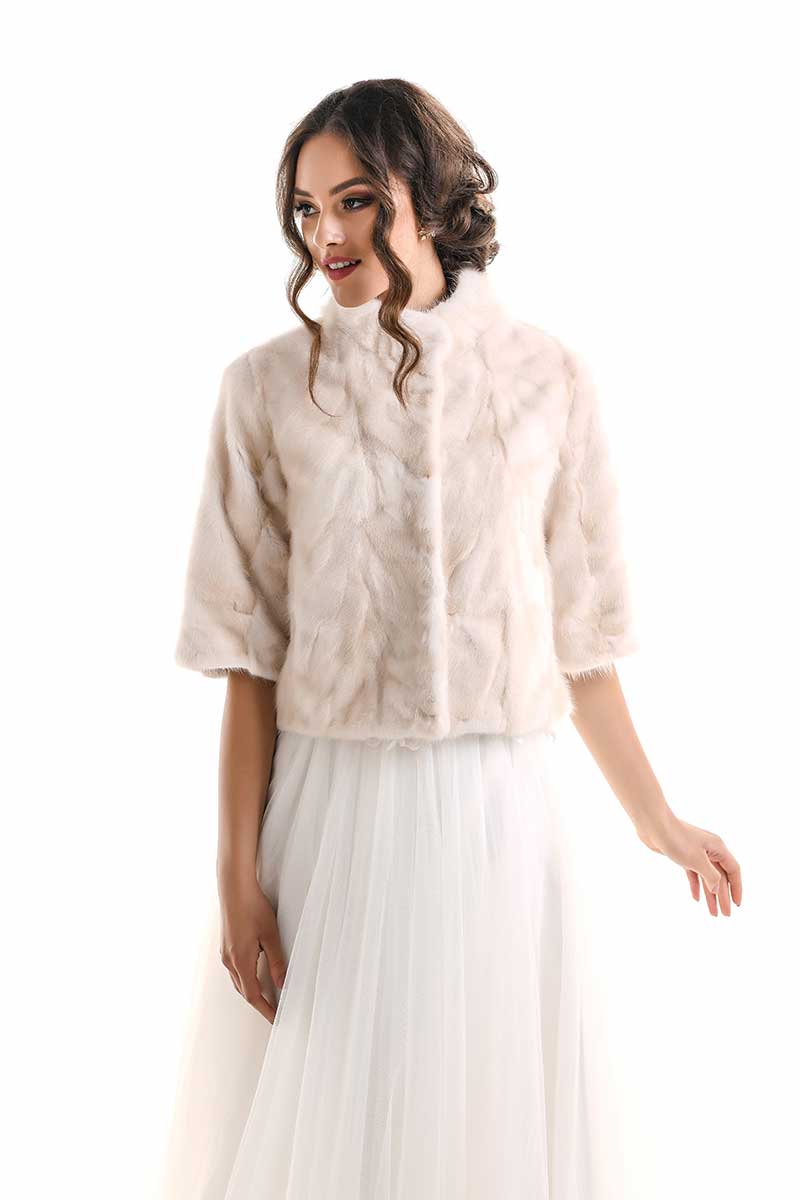 Woman wearing a beige fur jacket over a white dress on a white background