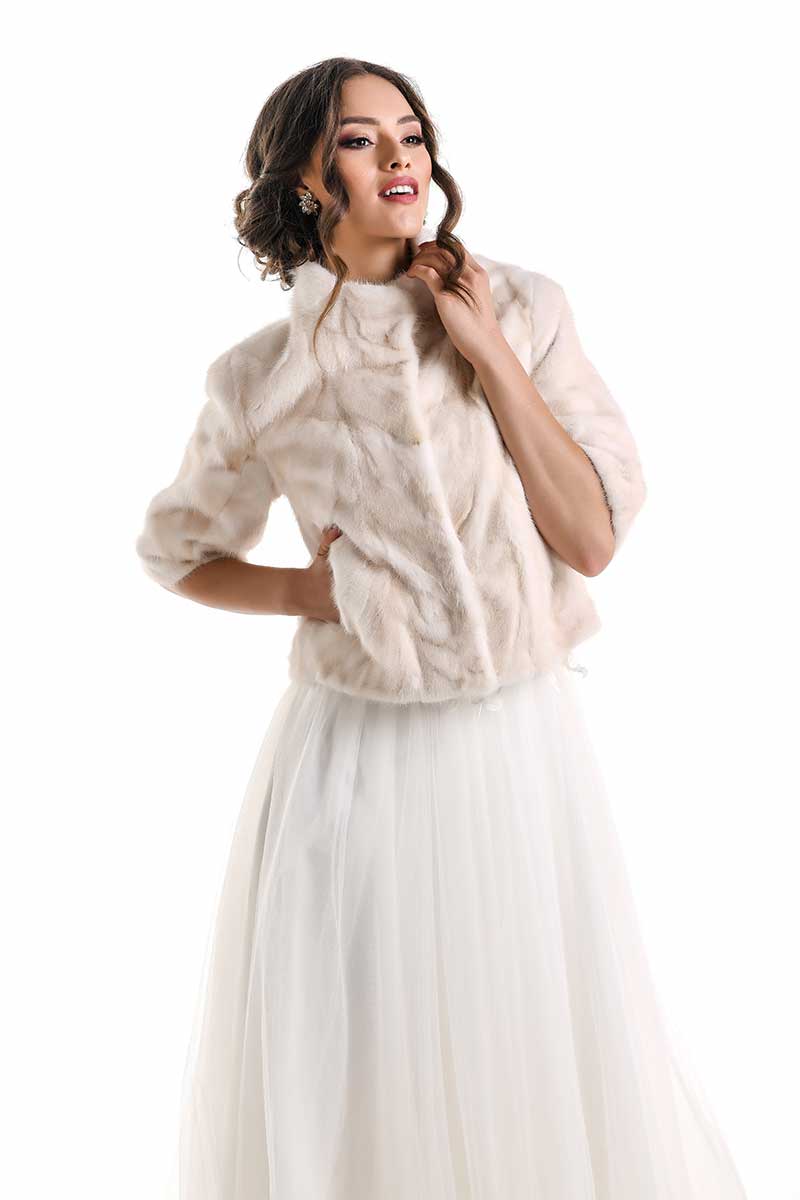 Woman wearing a beige fur jacket over a white dress on a white background