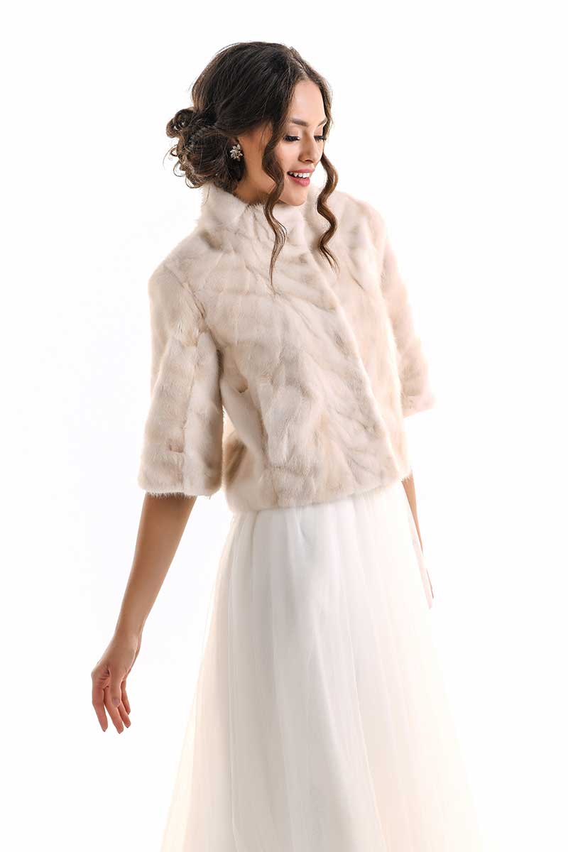 Woman wearing a beige fur jacket over a white dress on a white background