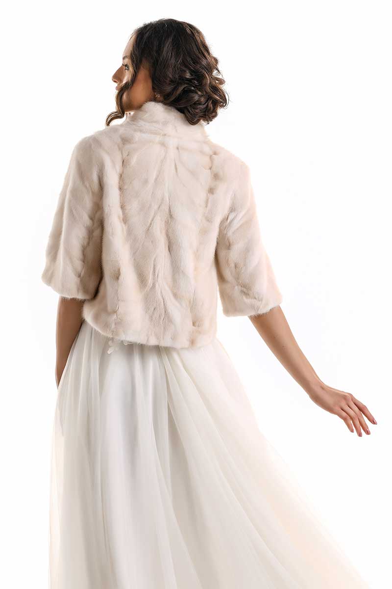 Woman wearing a beige fur jacket over a white dress on a white background