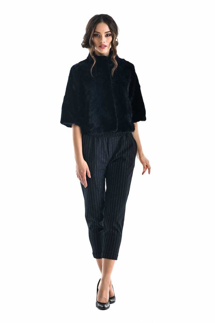 Woman wearing a navy fur jacket striped pants on a white background