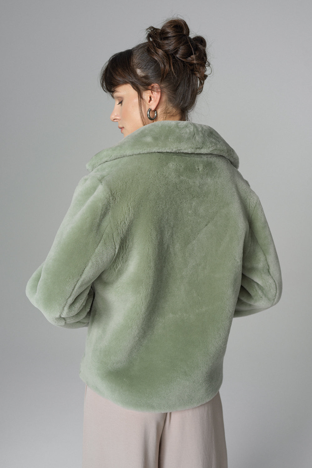 Person wearing a green fur coat against a gray background