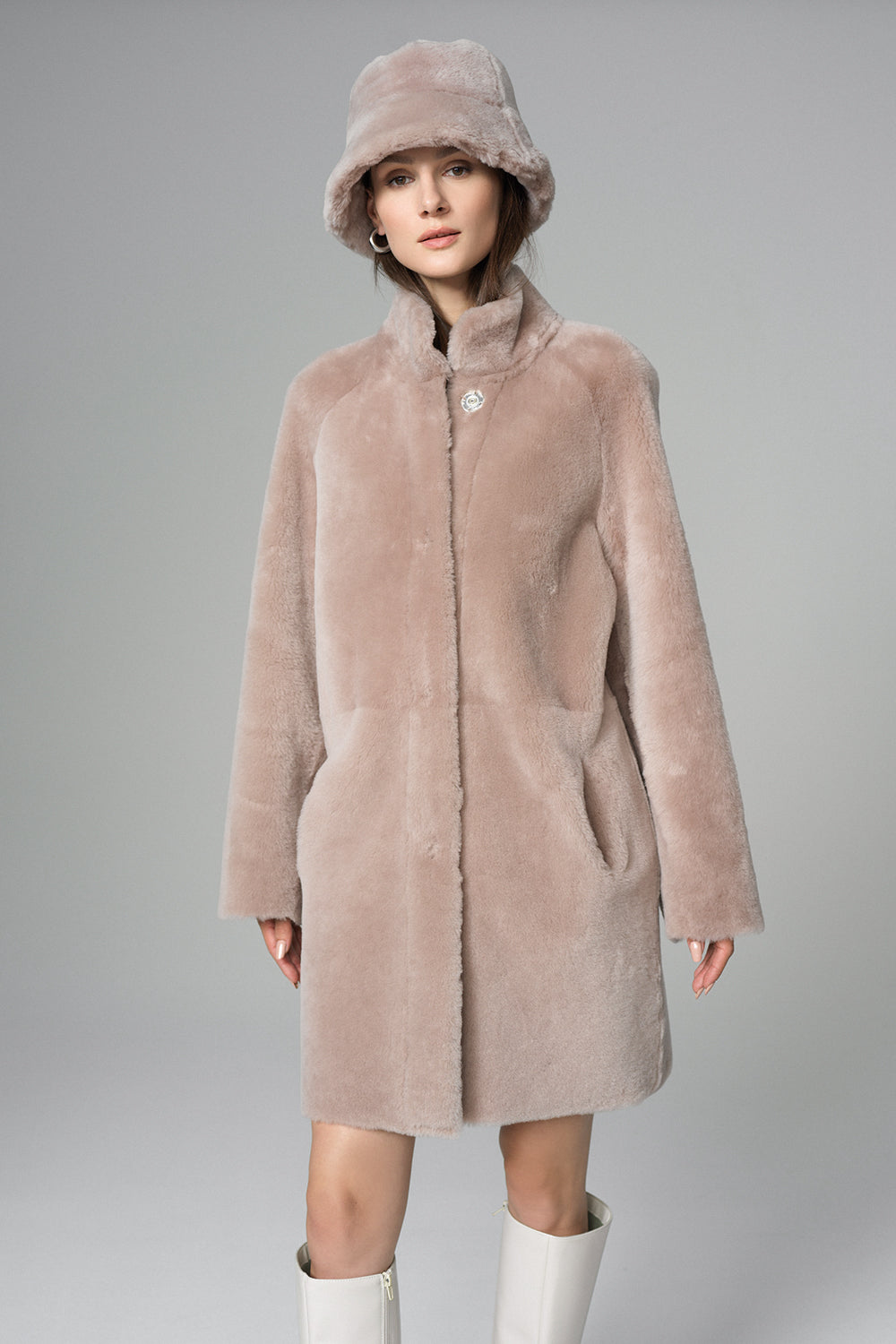 Woman wearing a pink fur coat and matching hat on a gray background
