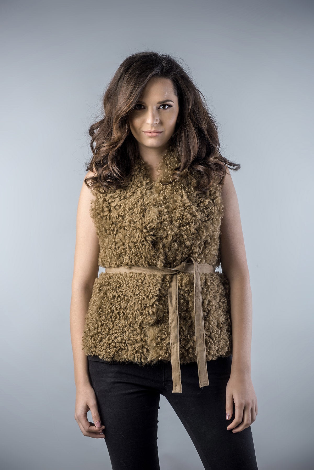 Woman wearing a brown textured vest with a belt against a gray background