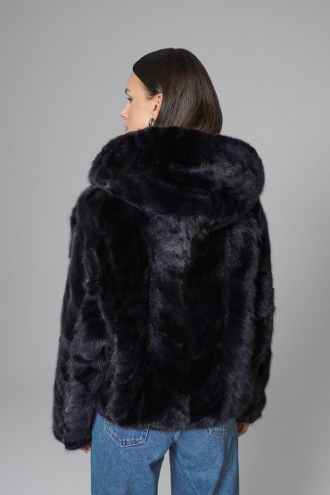 Person wearing a navy fur coat with a hood on a gray background