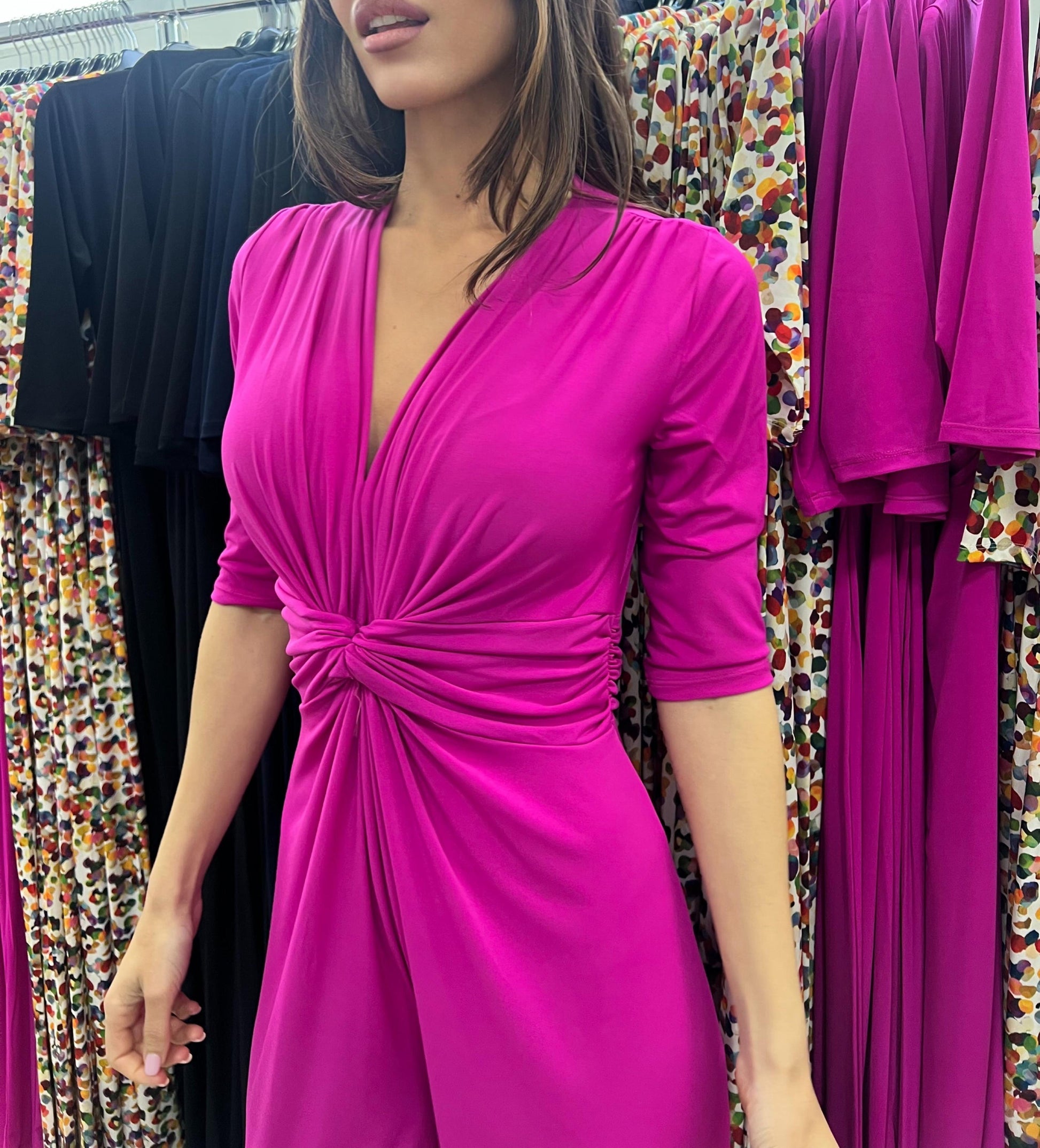 Woman wearing a bright pink dress with a knot detail in front of colorful fabric.