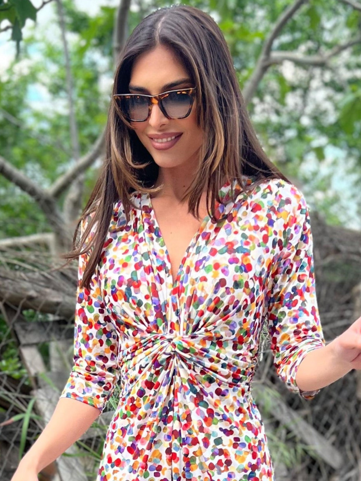 Woman in a colorful floral dress walking outdoors with greenery in the background