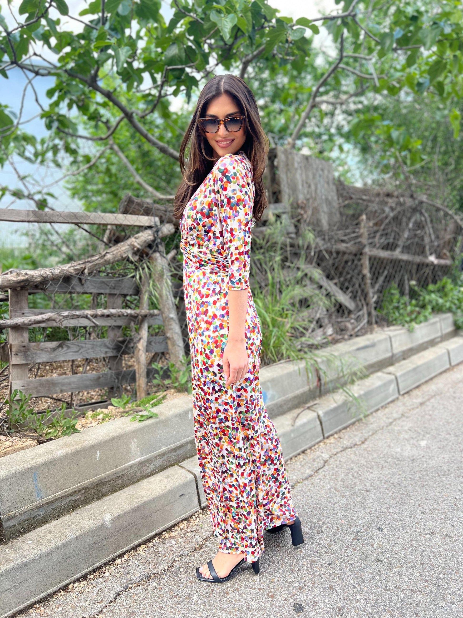 Woman in a colorful dress standing outdoors with greenery in the background
