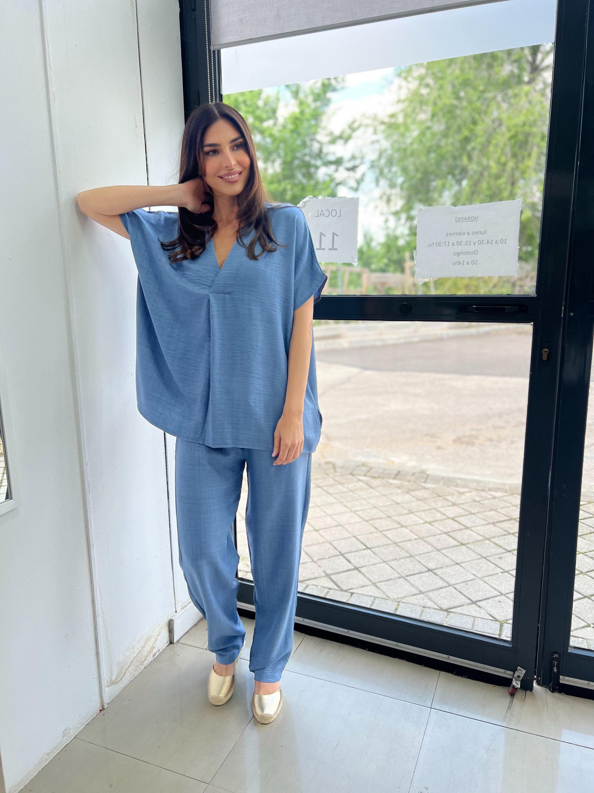 Woman in a blue outfit standing by a glass door.