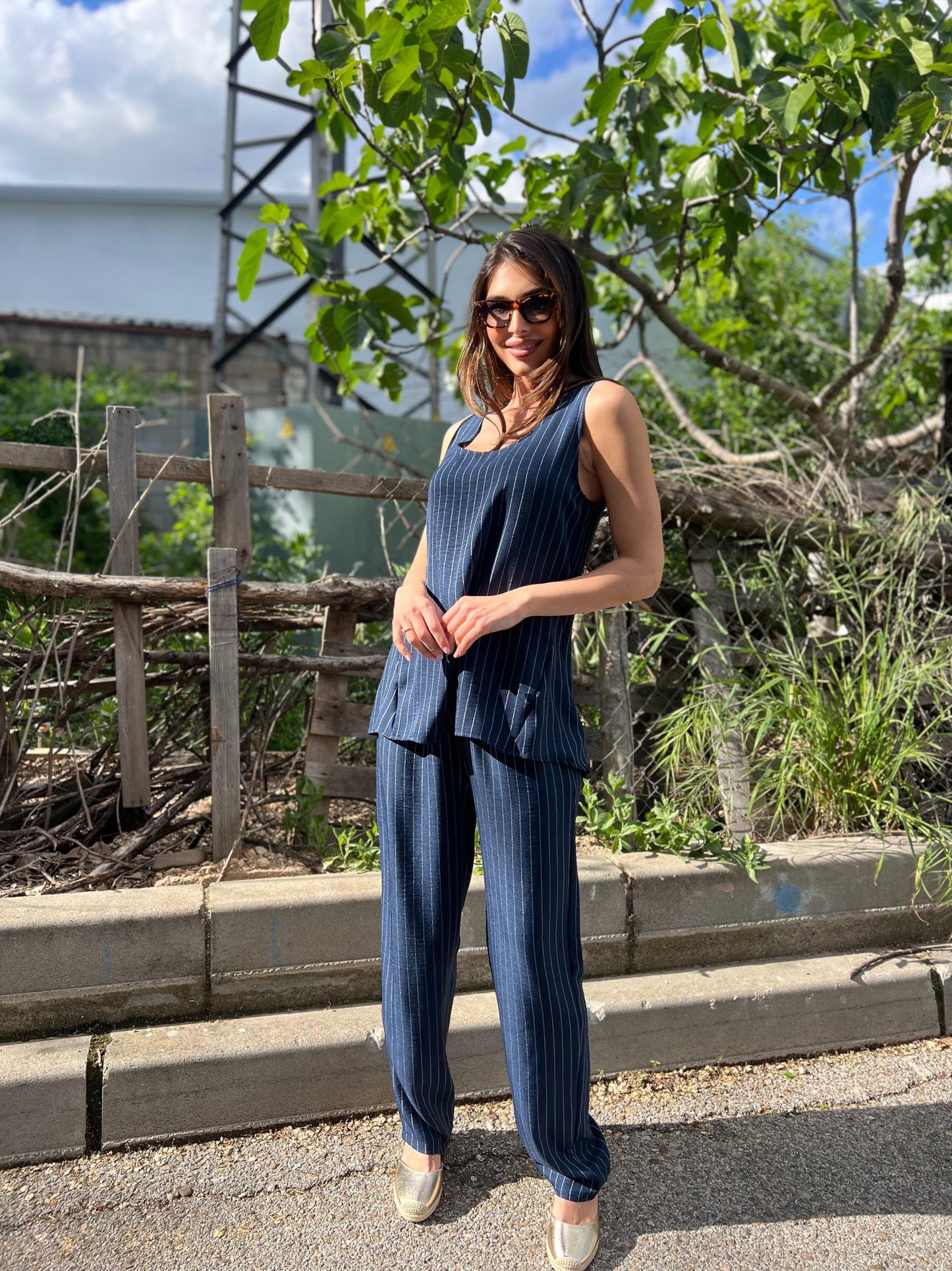 Woman in a blue outfit standing outdoors with greenery in the background