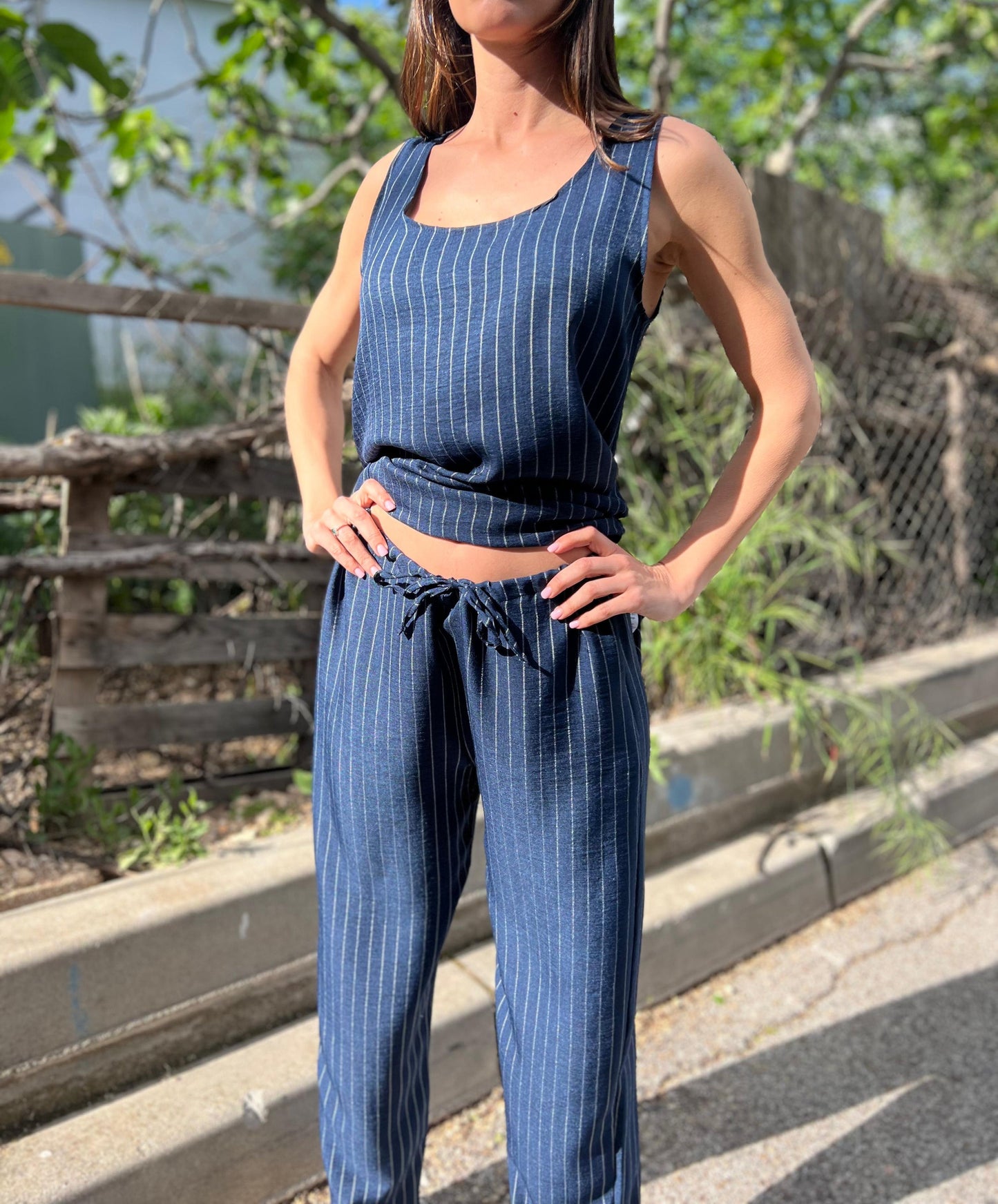 Woman wearing a blue pinstripe outfit standing outdoors with greenery in the background