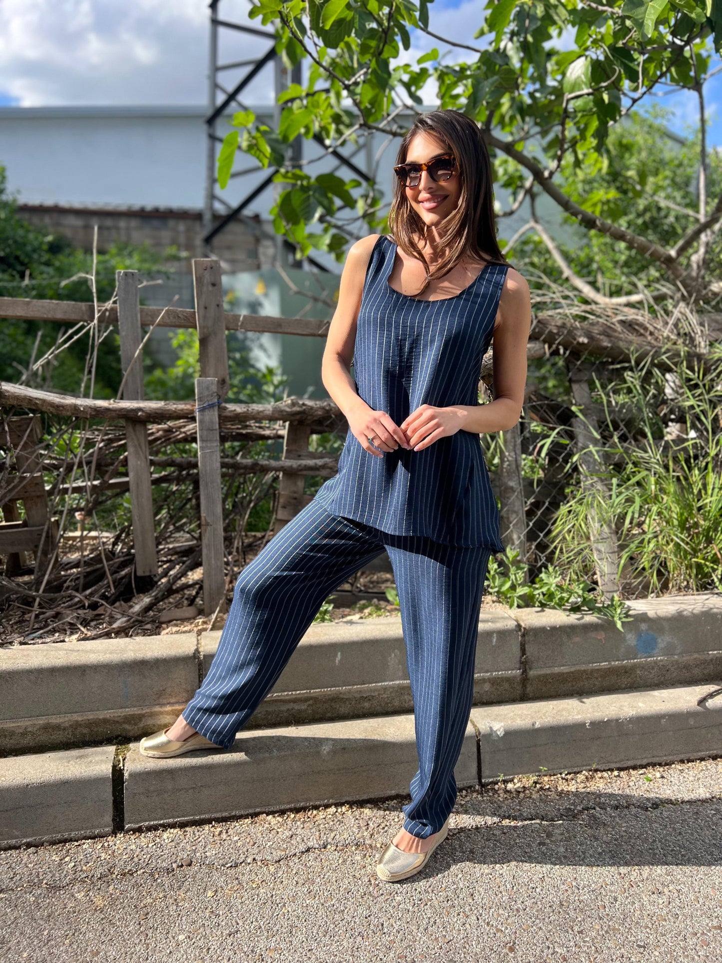 Woman in a blue outfit standing on steps with greenery in the background