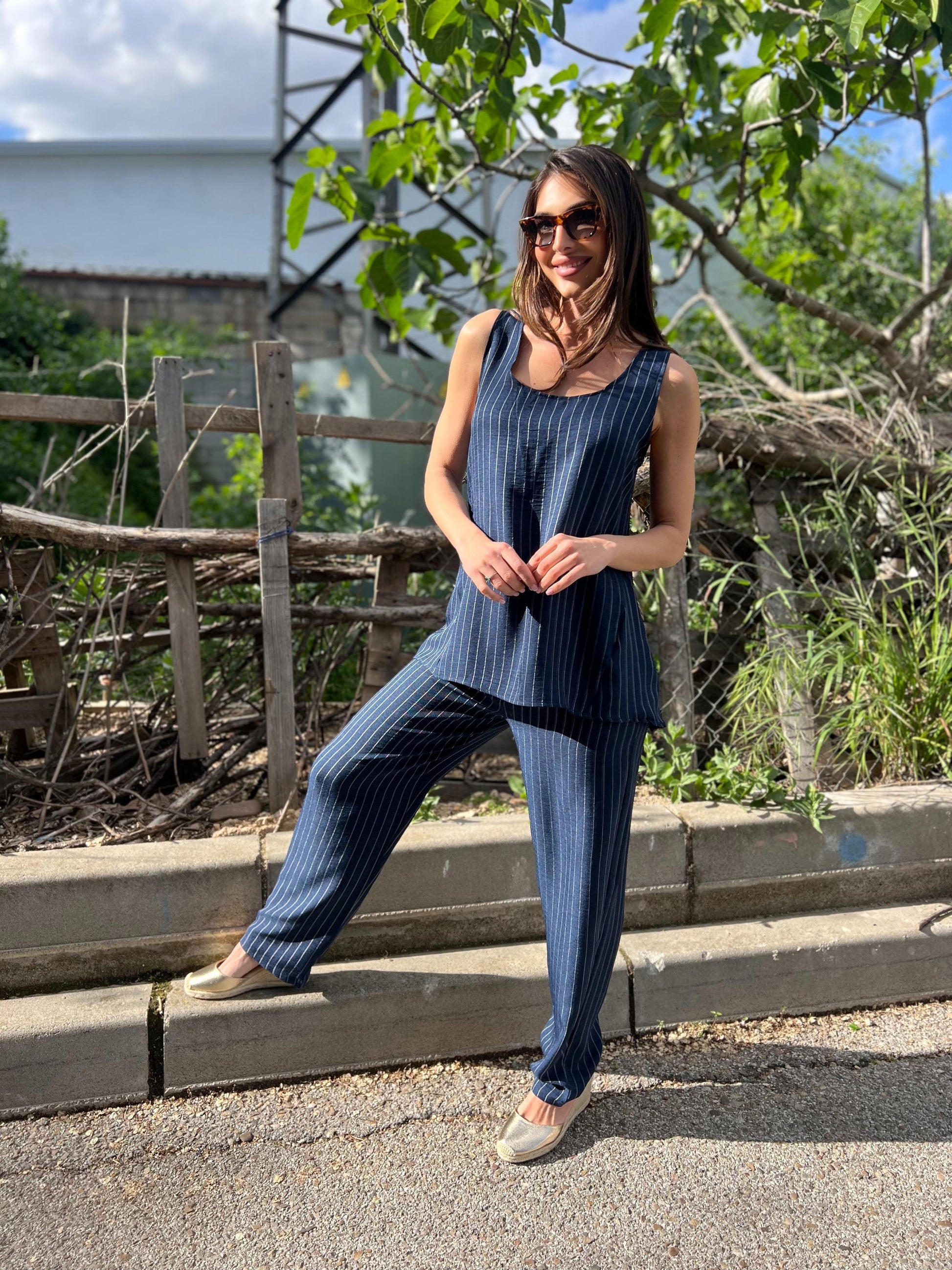 Woman in a blue outfit standing on steps with greenery in the background