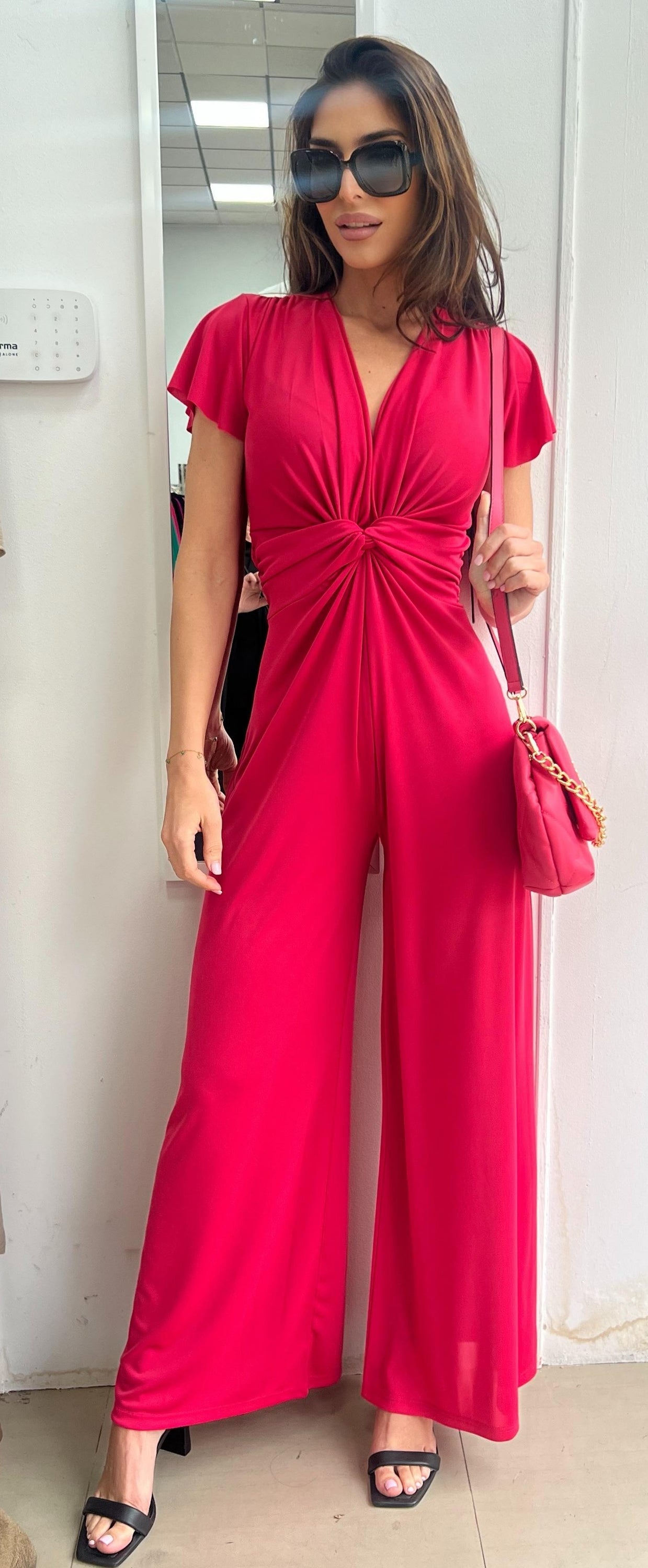 Woman wearing a bright pink jumpsuit with a matching handbag indoors.
