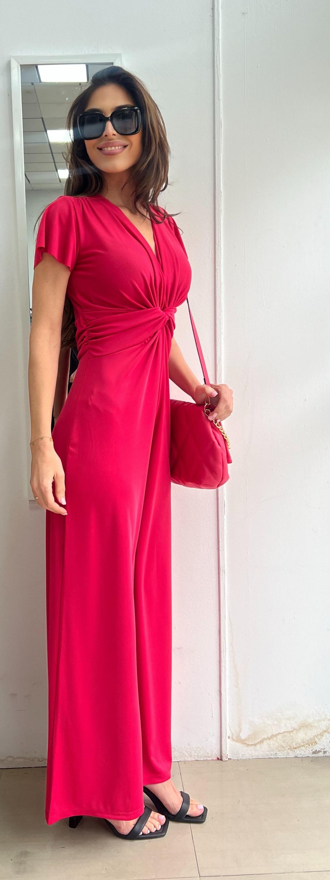 Woman wearing a bright pink dress and sunglasses indoors.