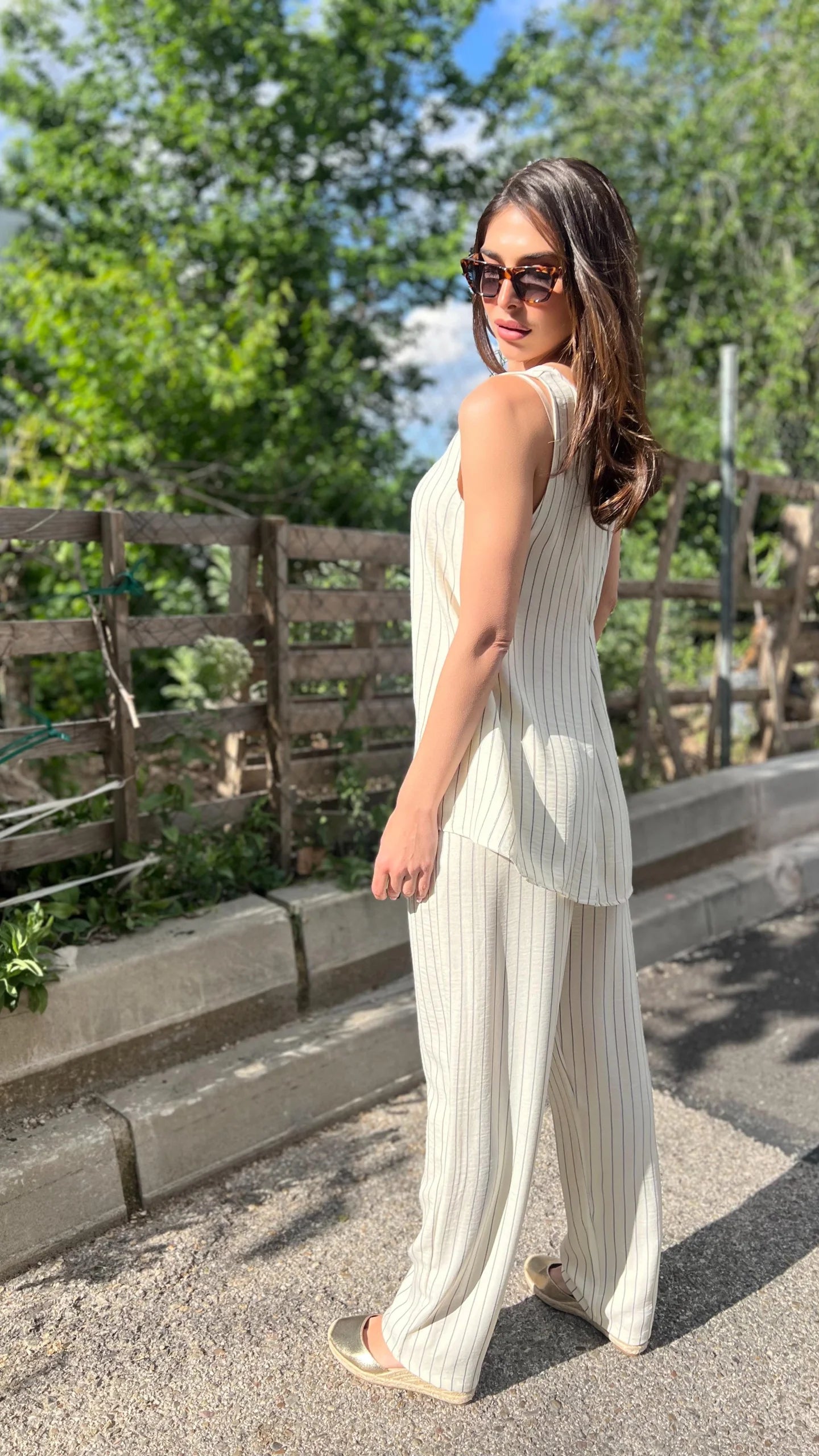 Woman in a white outfit standing outdoors with greenery in the background