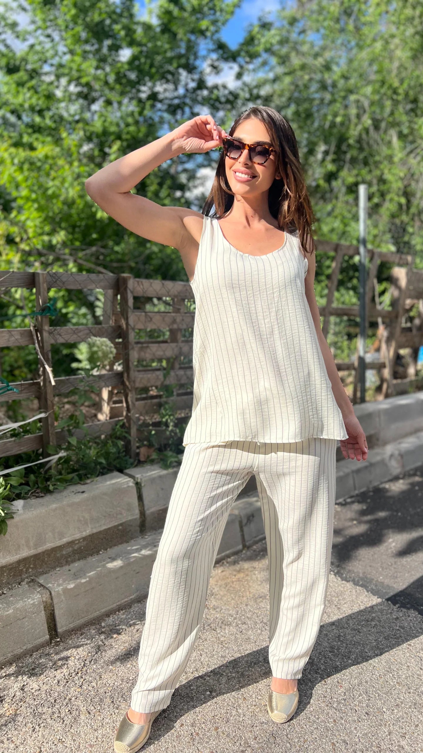 Woman in a white outfit standing outdoors with greenery in the background