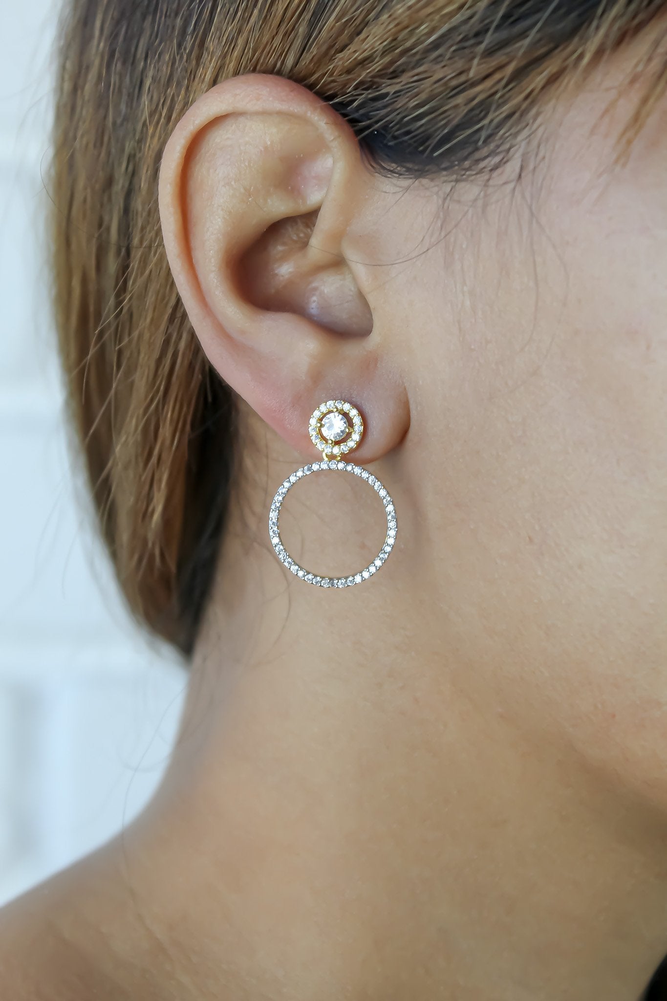 Close-up of an ear wearing a gold and silver hoop earring against a neutral background