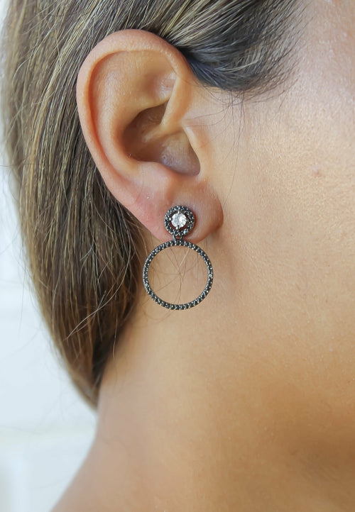 Close-up of an ear wearing a silver hoop earring with a gemstone on a plain background