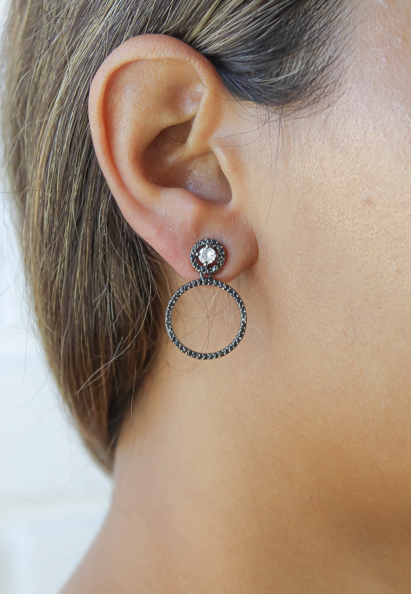 Close-up of an ear wearing a hoop earring with a gemstone on a plain background