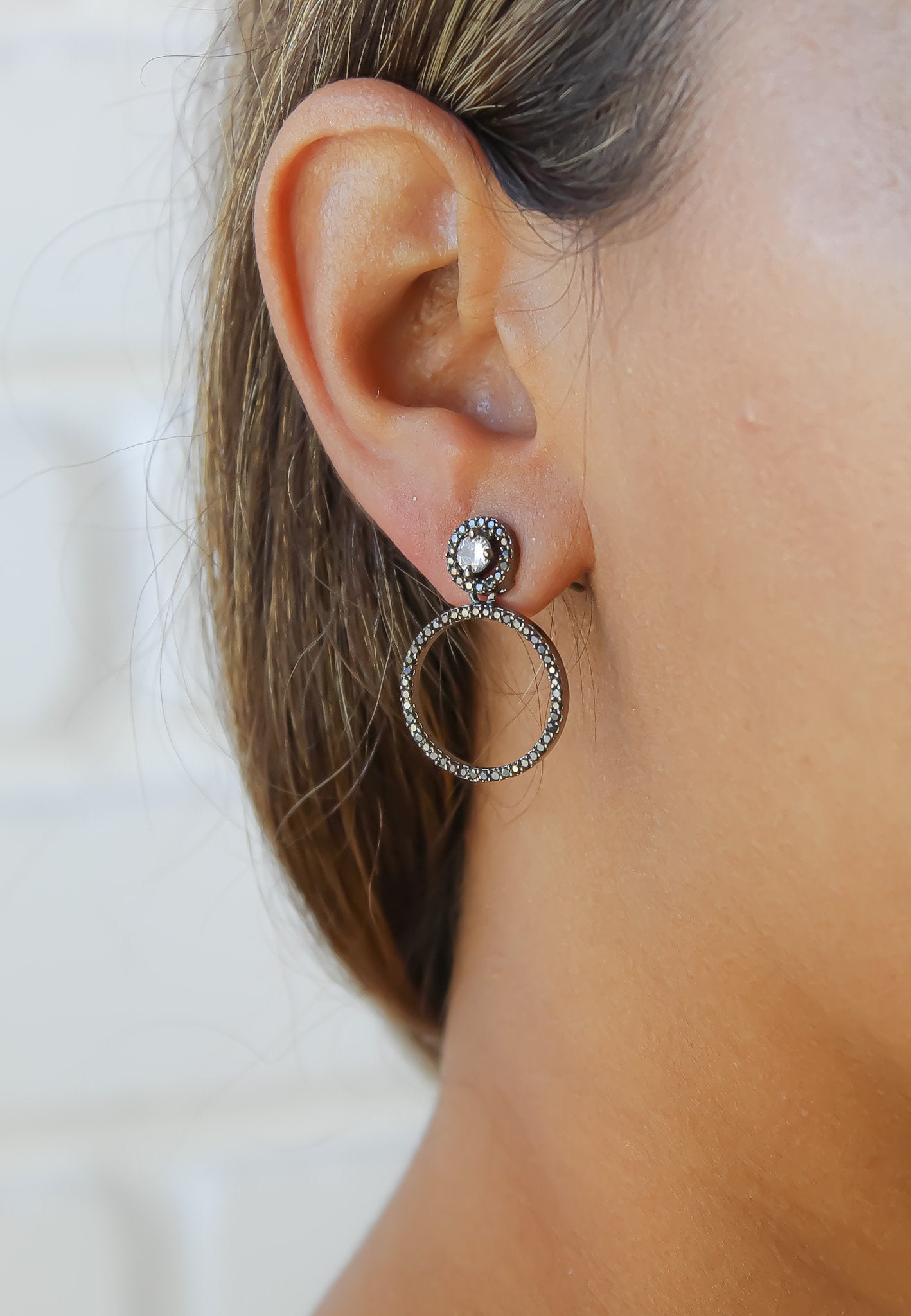 Close-up of an ear wearing a silver hoop earring with a white background