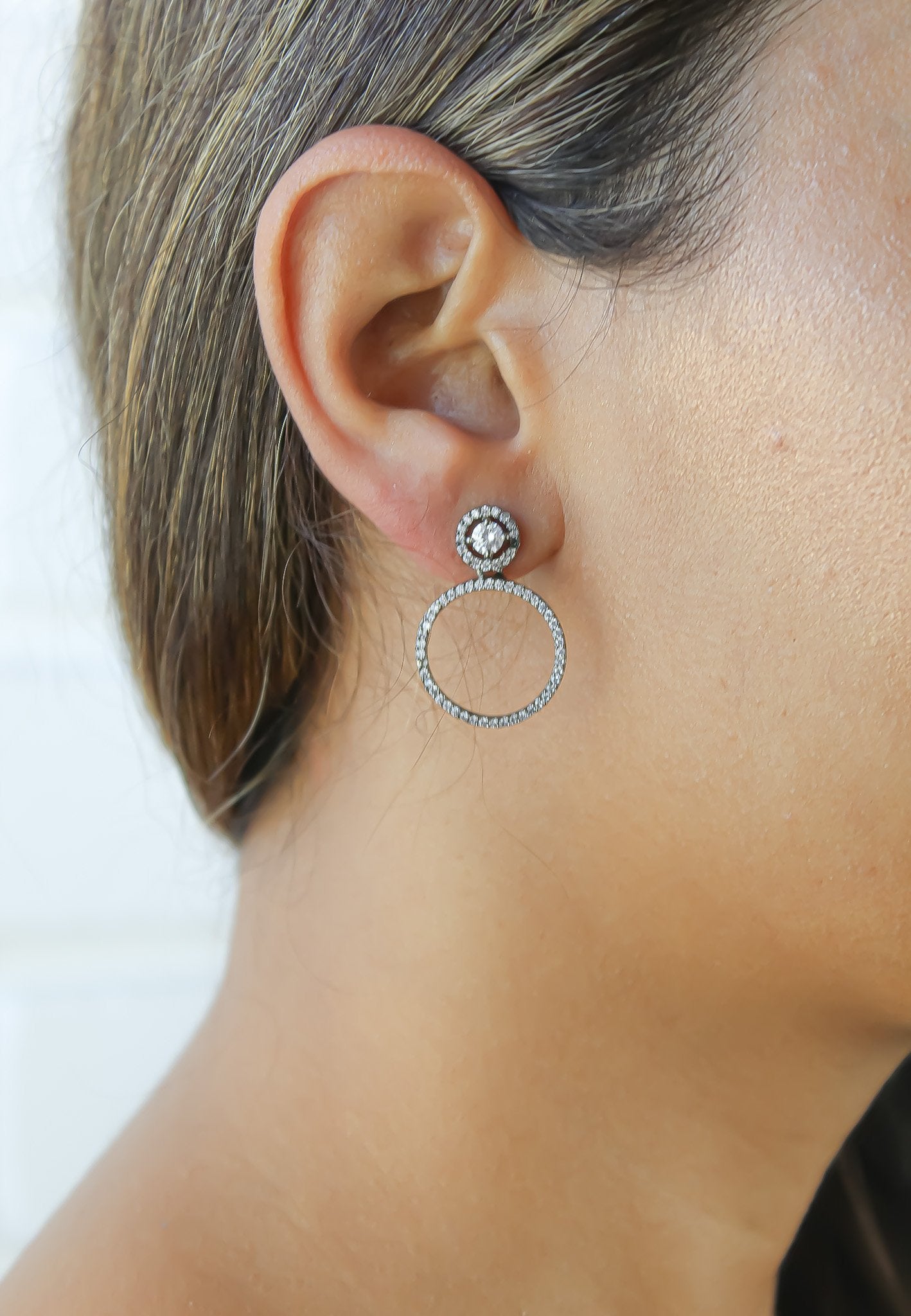 Close-up of an ear wearing a silver hoop earring with a central gemstone on a white background
