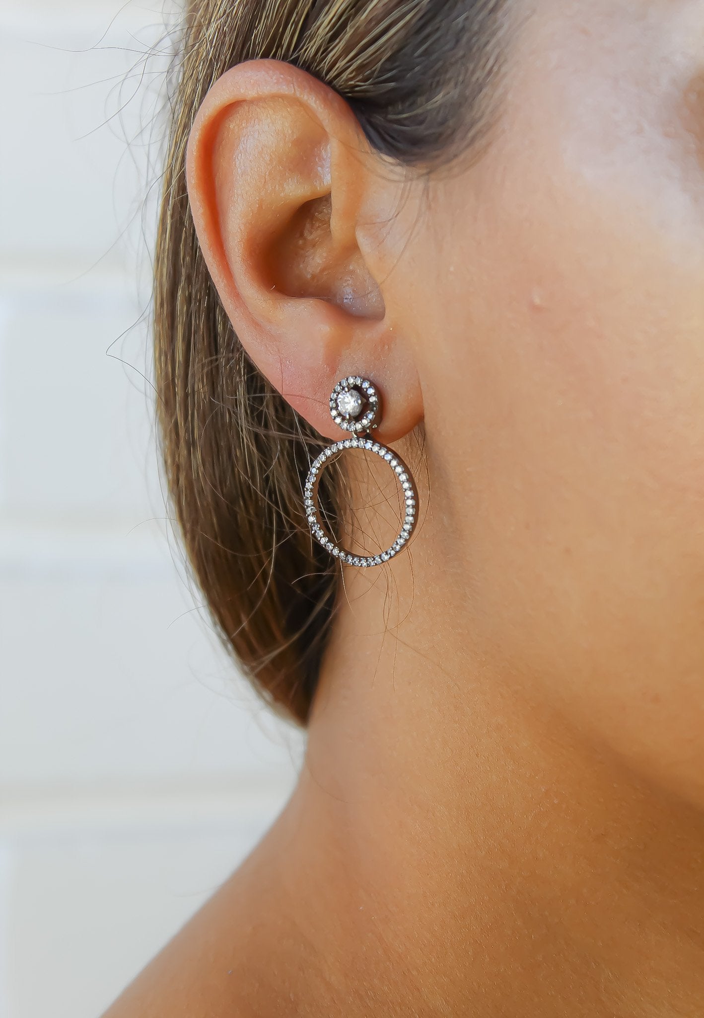 Close-up of an ear wearing a silver hoop earring with a small round gemstone.