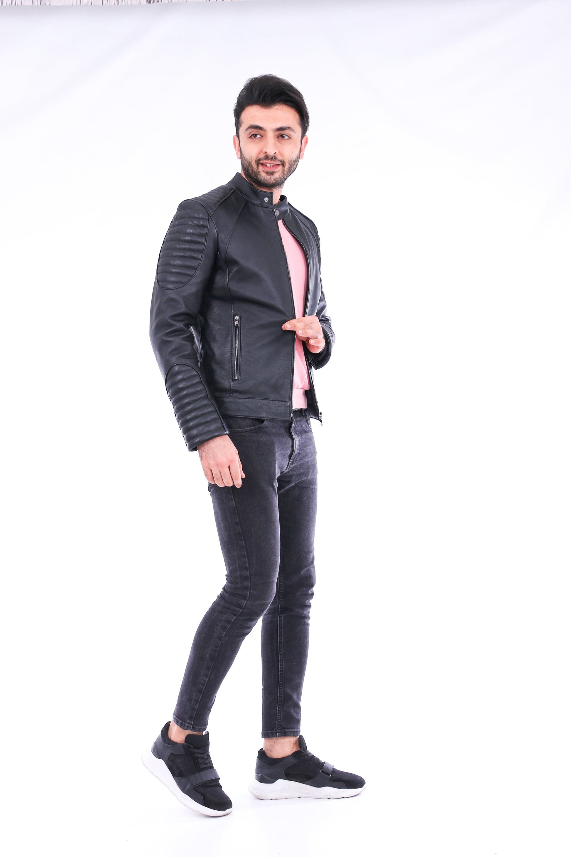 Man wearing a black leather jacket and gray jeans on a white background