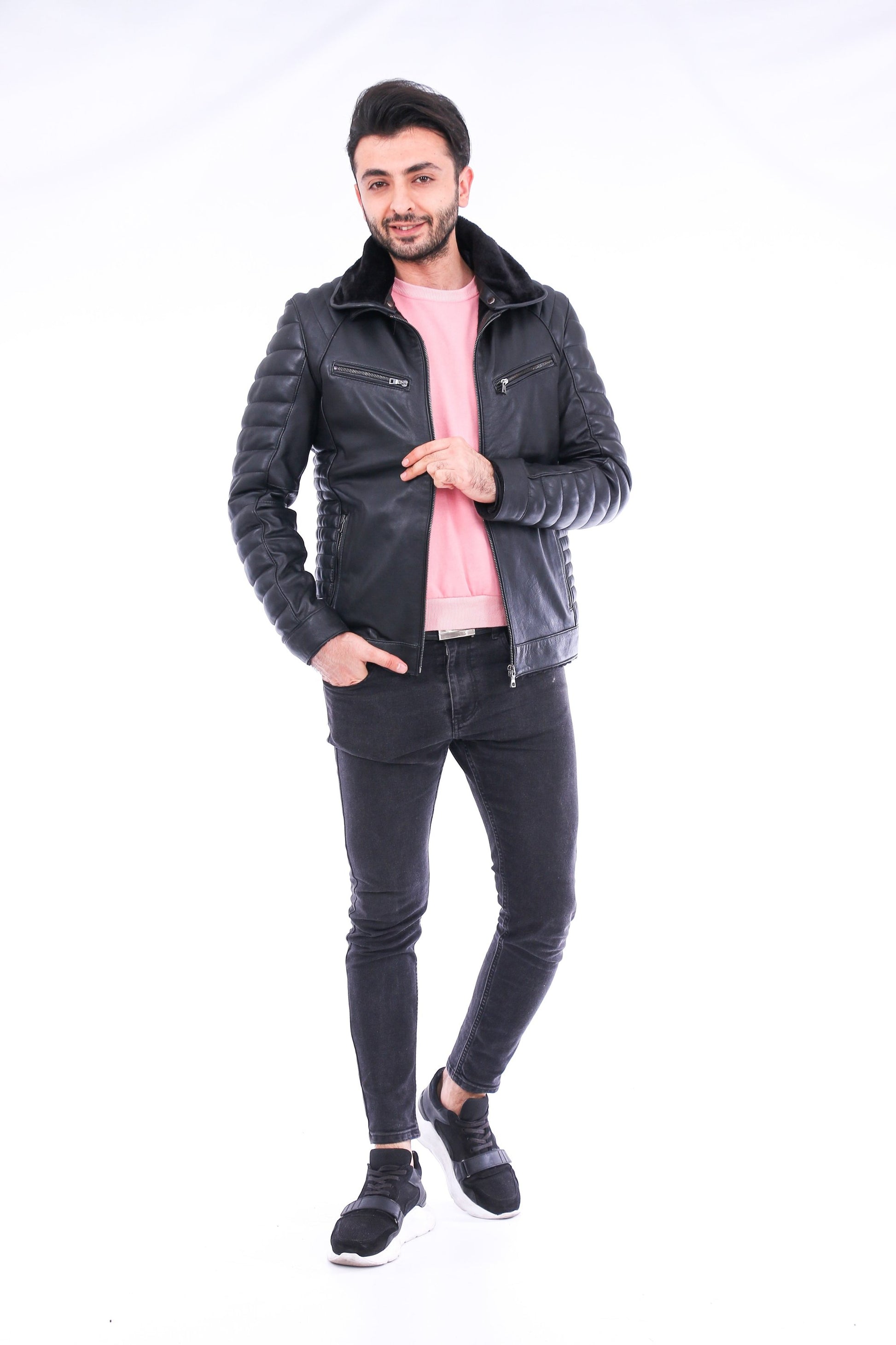 Man wearing a black leather jacket, pink shirt, and black jeans on a white background