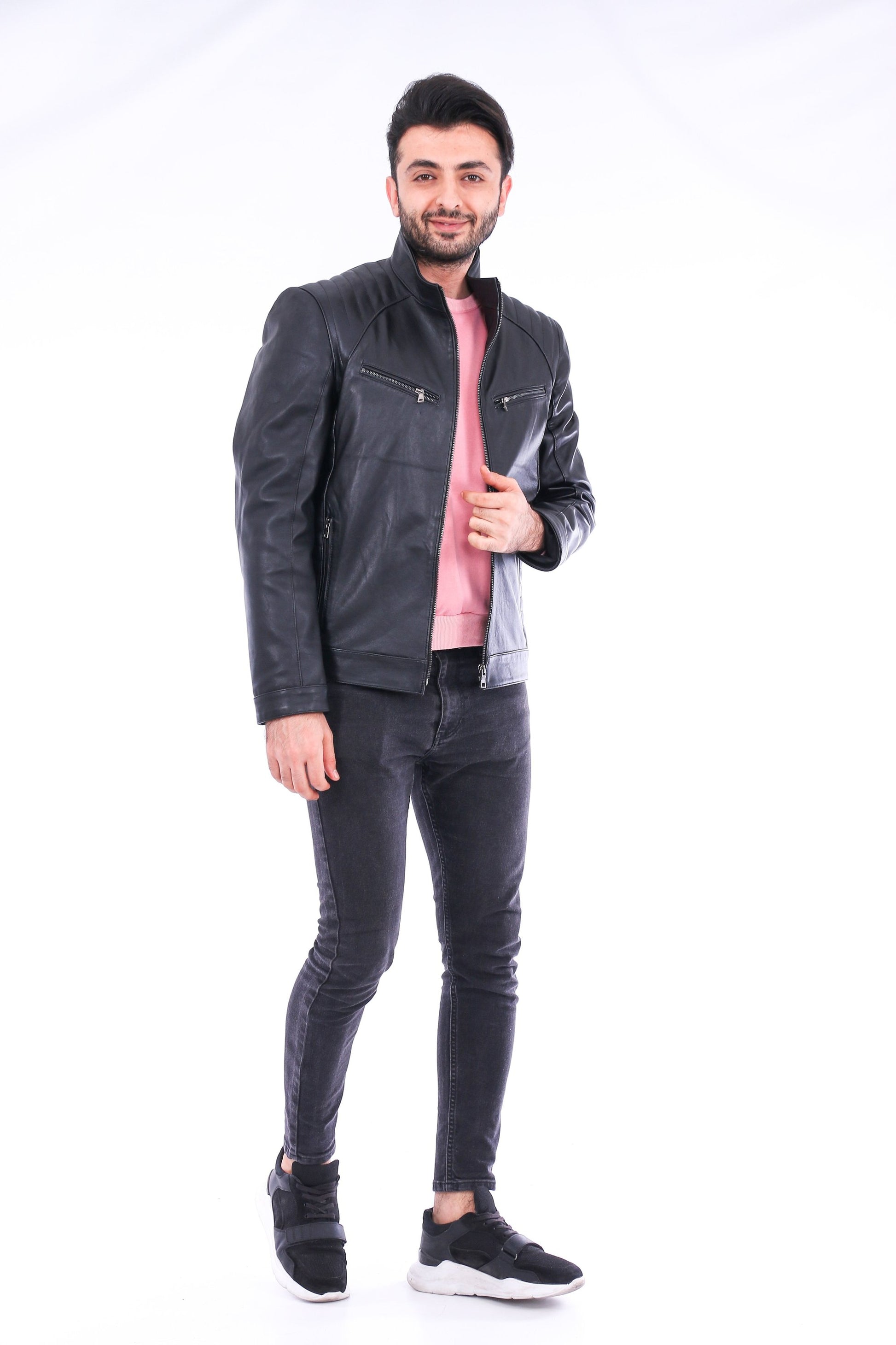 Man wearing a black leather jacket, pink shirt, and dark jeans on a white background