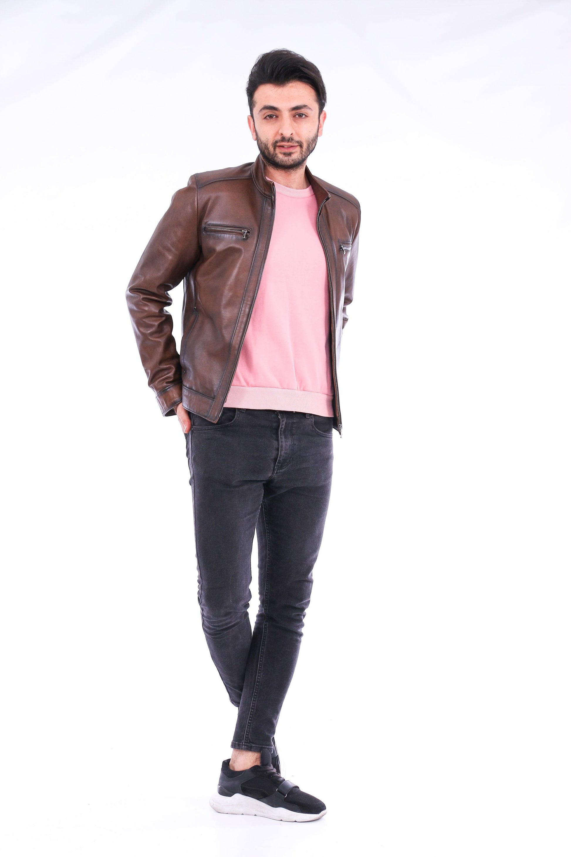 Man wearing a brown leather jacket, pink shirt, and black jeans on a white background