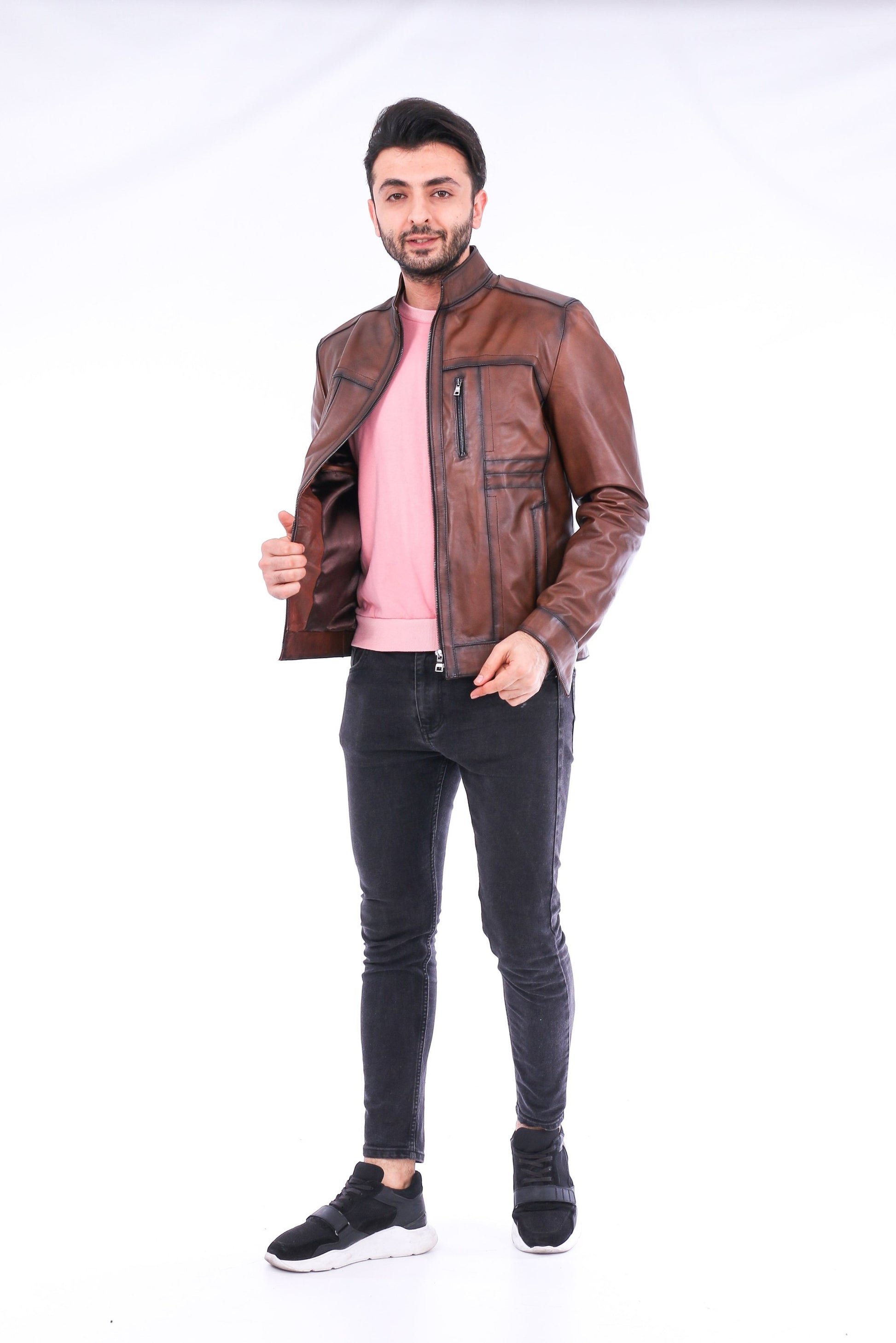 Man wearing a brown leather jacket, pink shirt, and black jeans on a white background