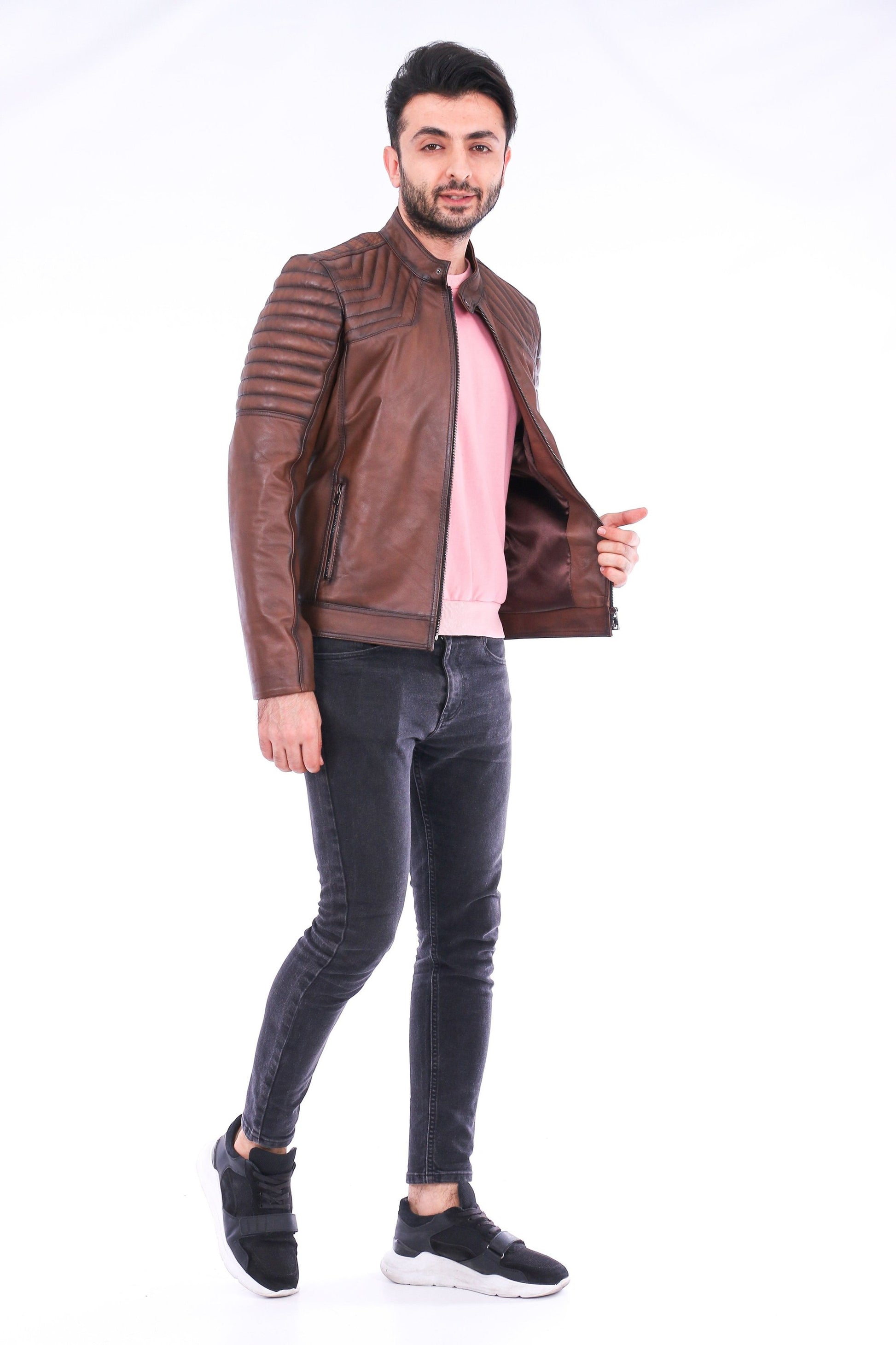 Man wearing a brown leather jacket, pink shirt, and gray jeans on a white background
