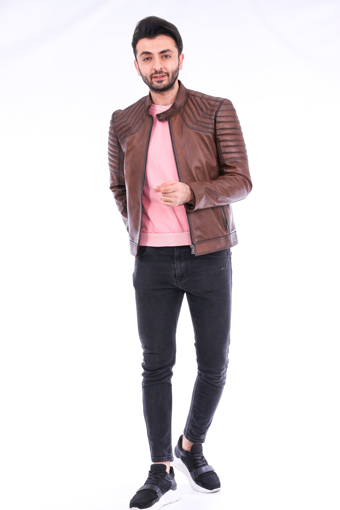 Man wearing a brown leather jacket, pink shirt, and black jeans on a white background