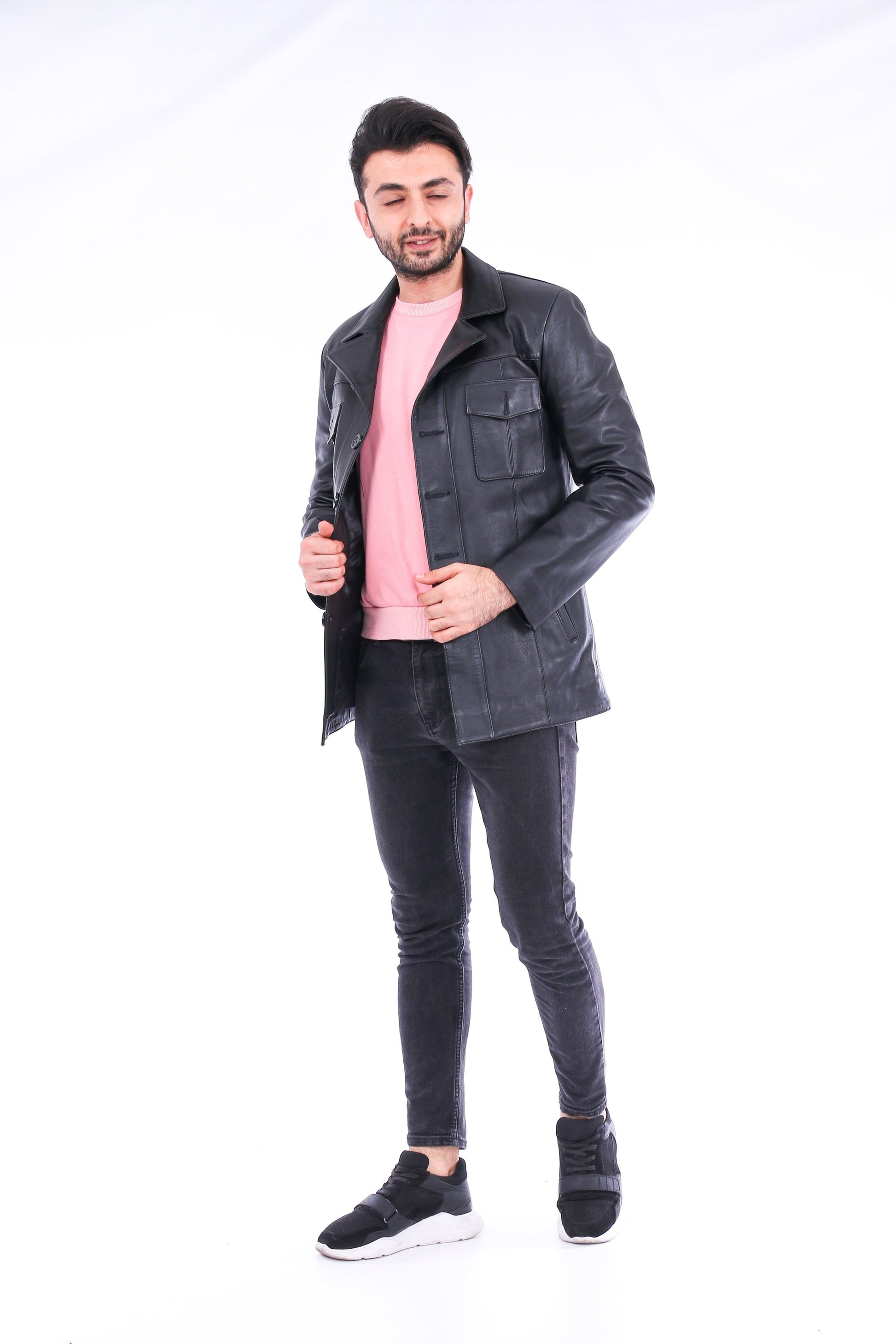 Man wearing a black leather jacket, pink shirt, and black pants on a white background
