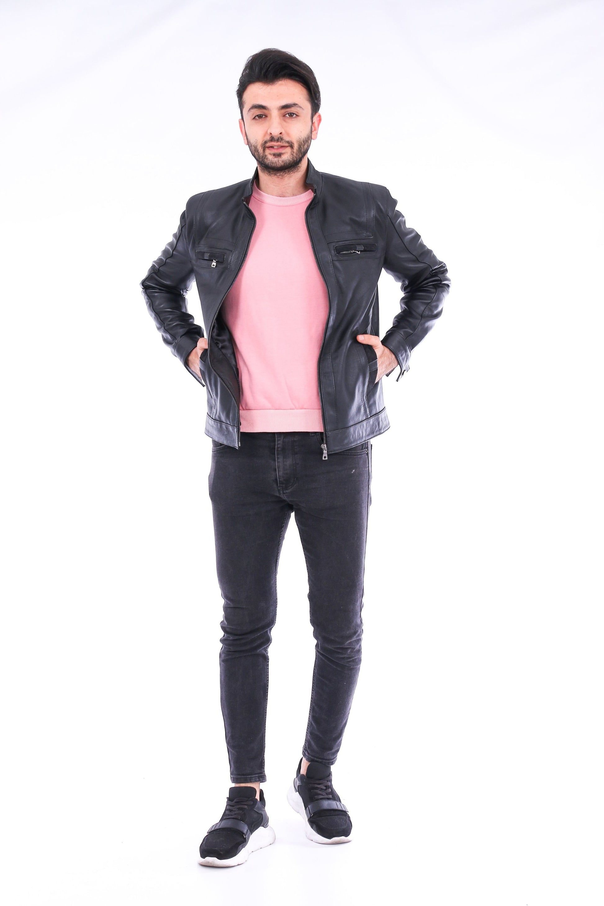 Man wearing a black jacket, pink shirt, and black jeans on a white background