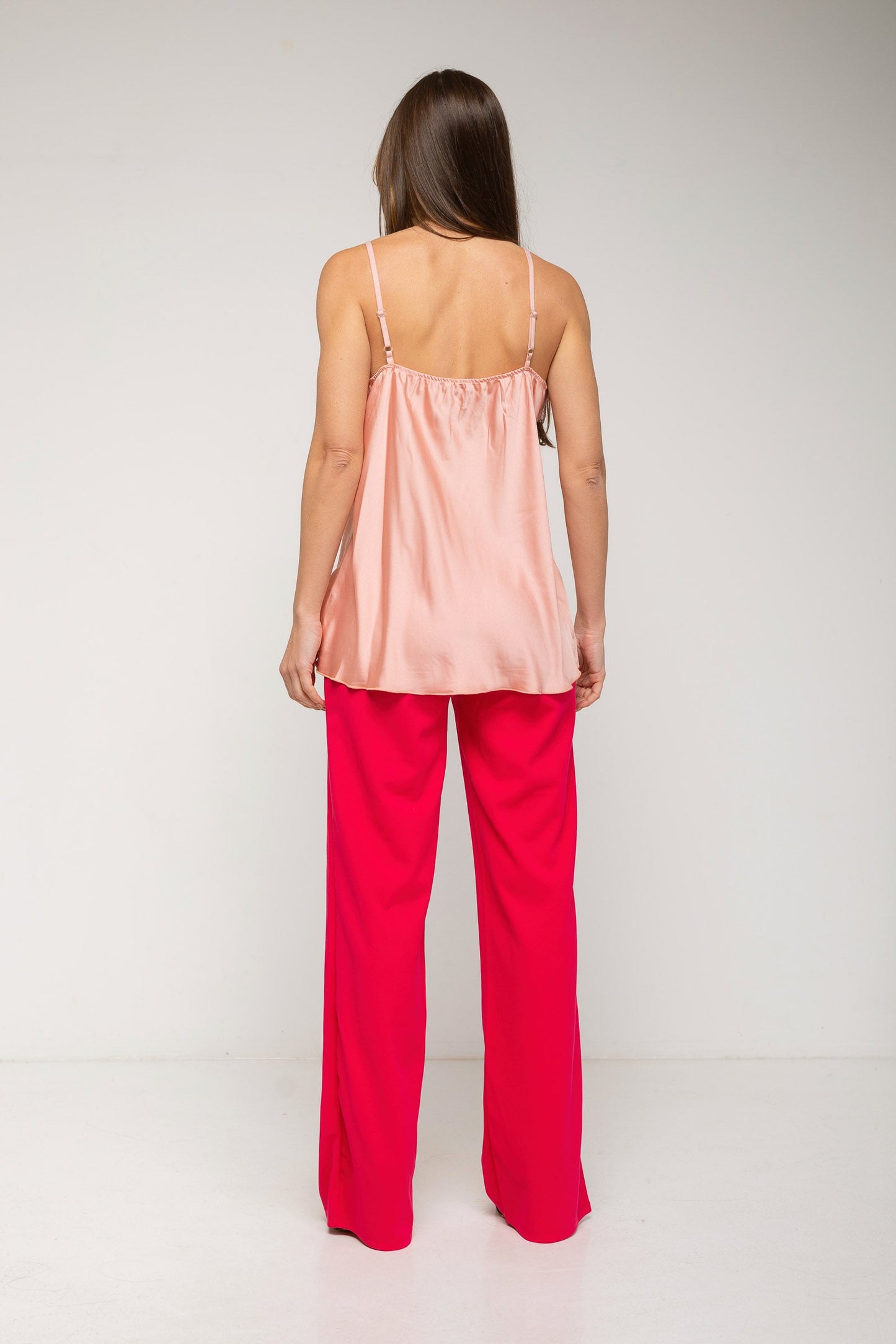 Woman wearing a pink satin top and red pants on a white background