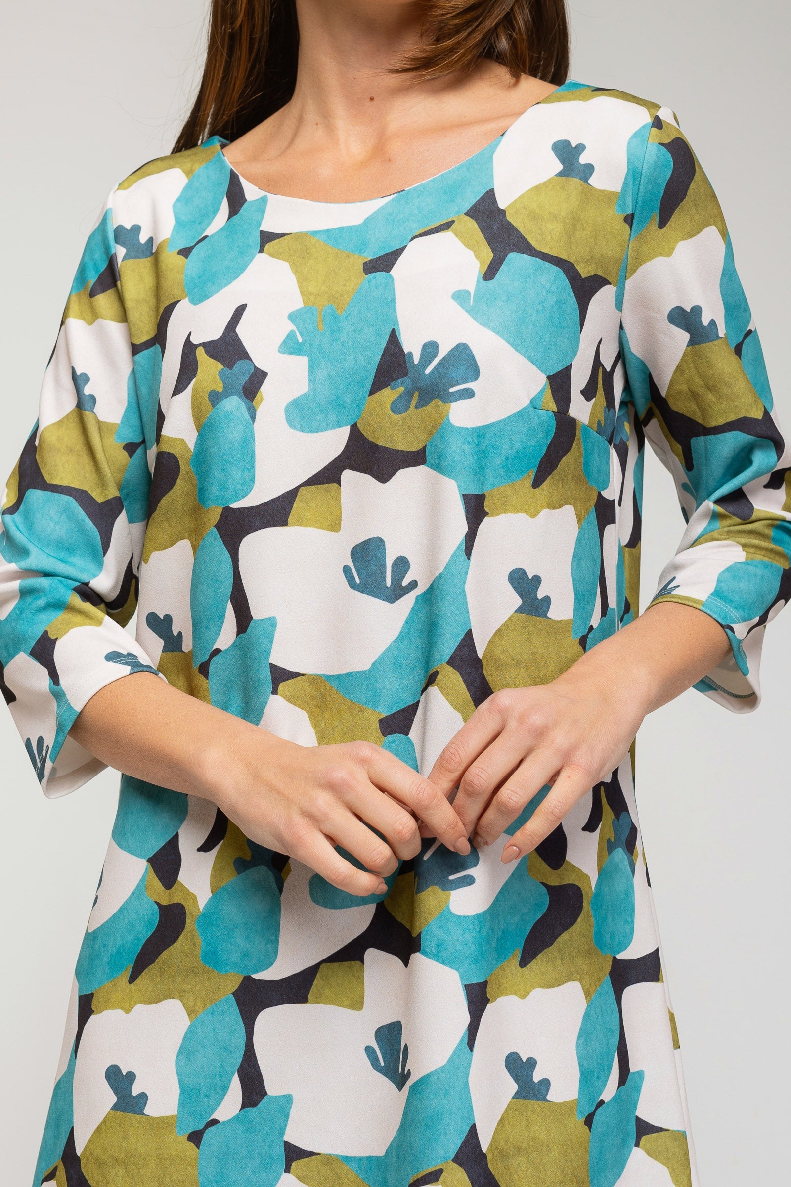 Woman wearing a floral patterned dress with green, blue, and white colors on a plain background