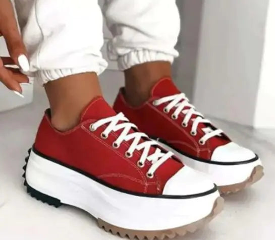 Red sneakers with white soles worn by a person on a light background