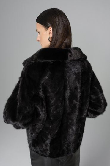Person wearing a black fur coat against a gray background