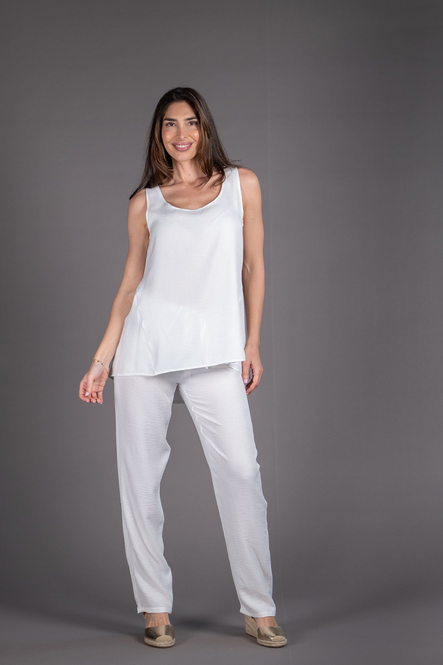 Woman wearing a white sleeveless top and pants against a gray background