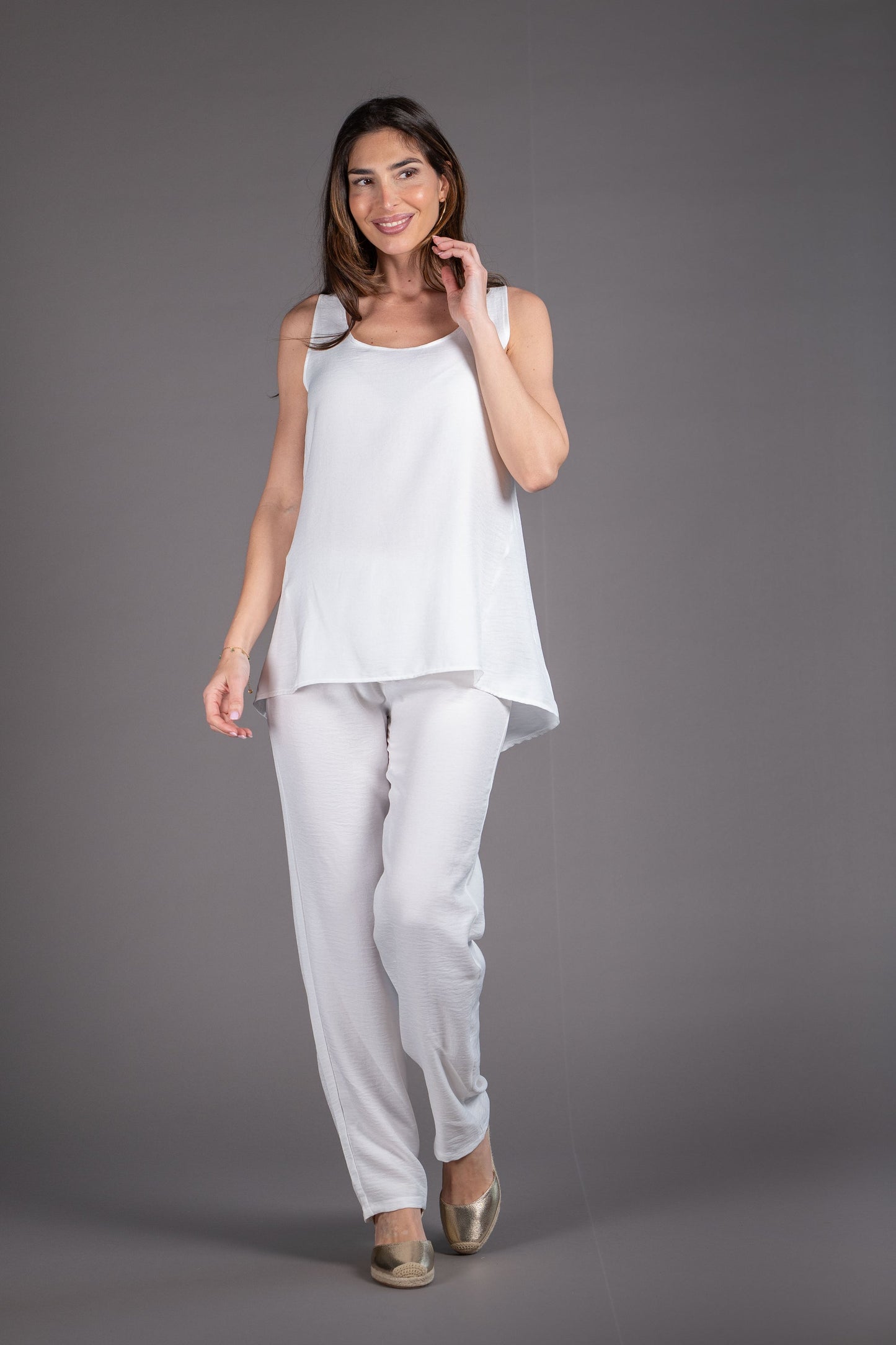 Woman wearing a white sleeveless top and pants on a gray background