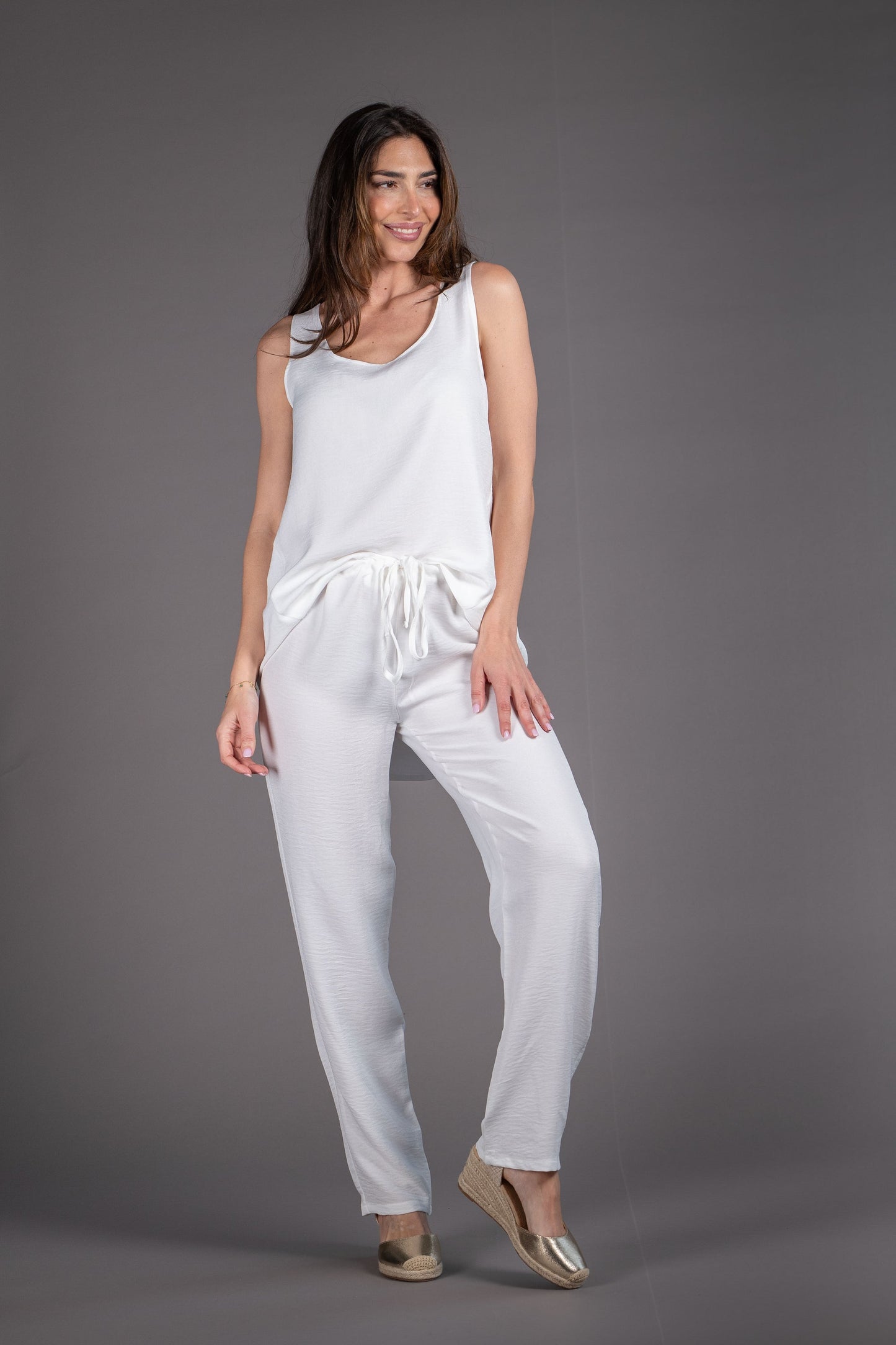 Woman wearing a white sleeveless top and pants on a gray background