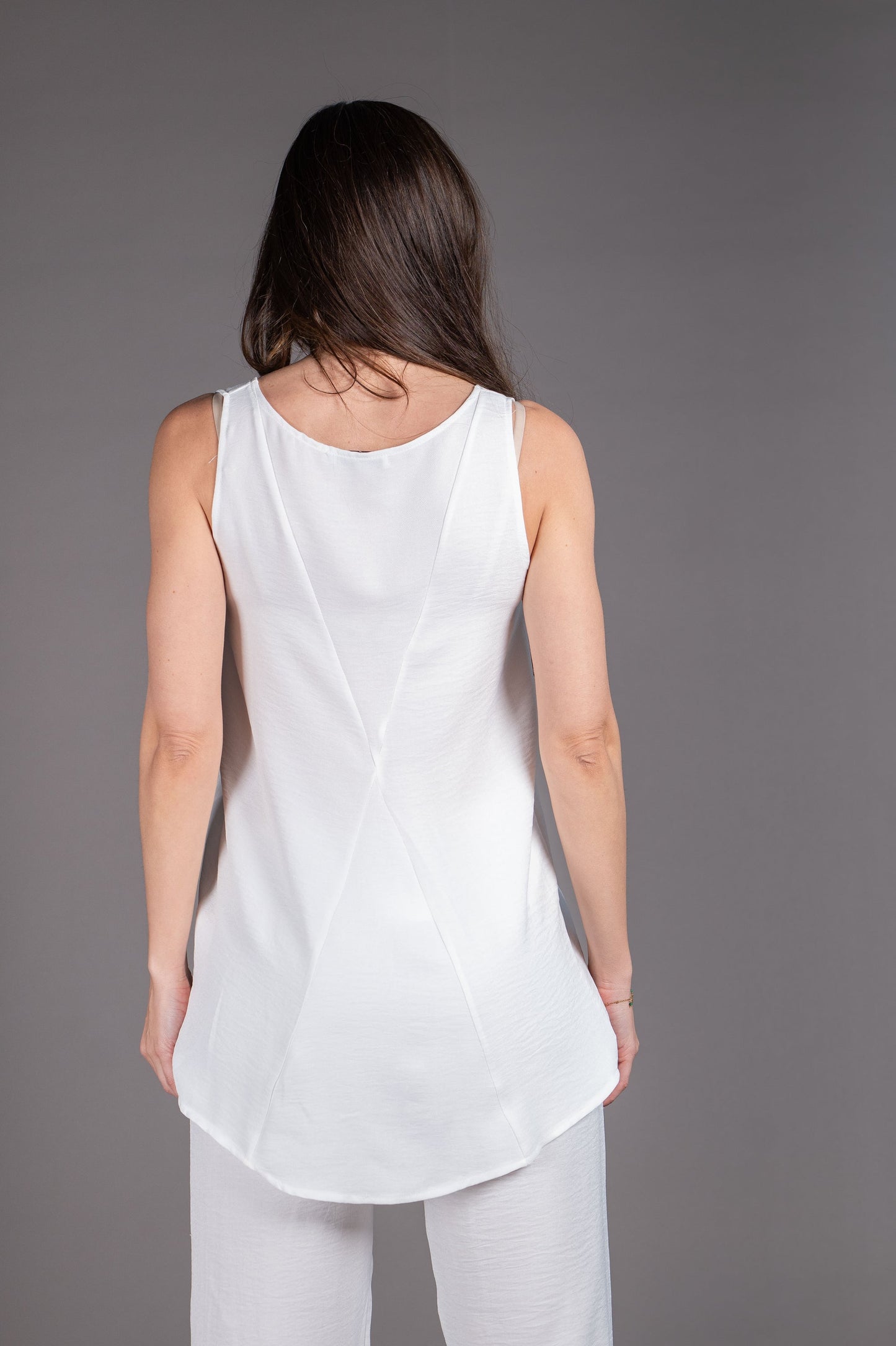 Woman wearing a white sleeveless top and pants against a gray background