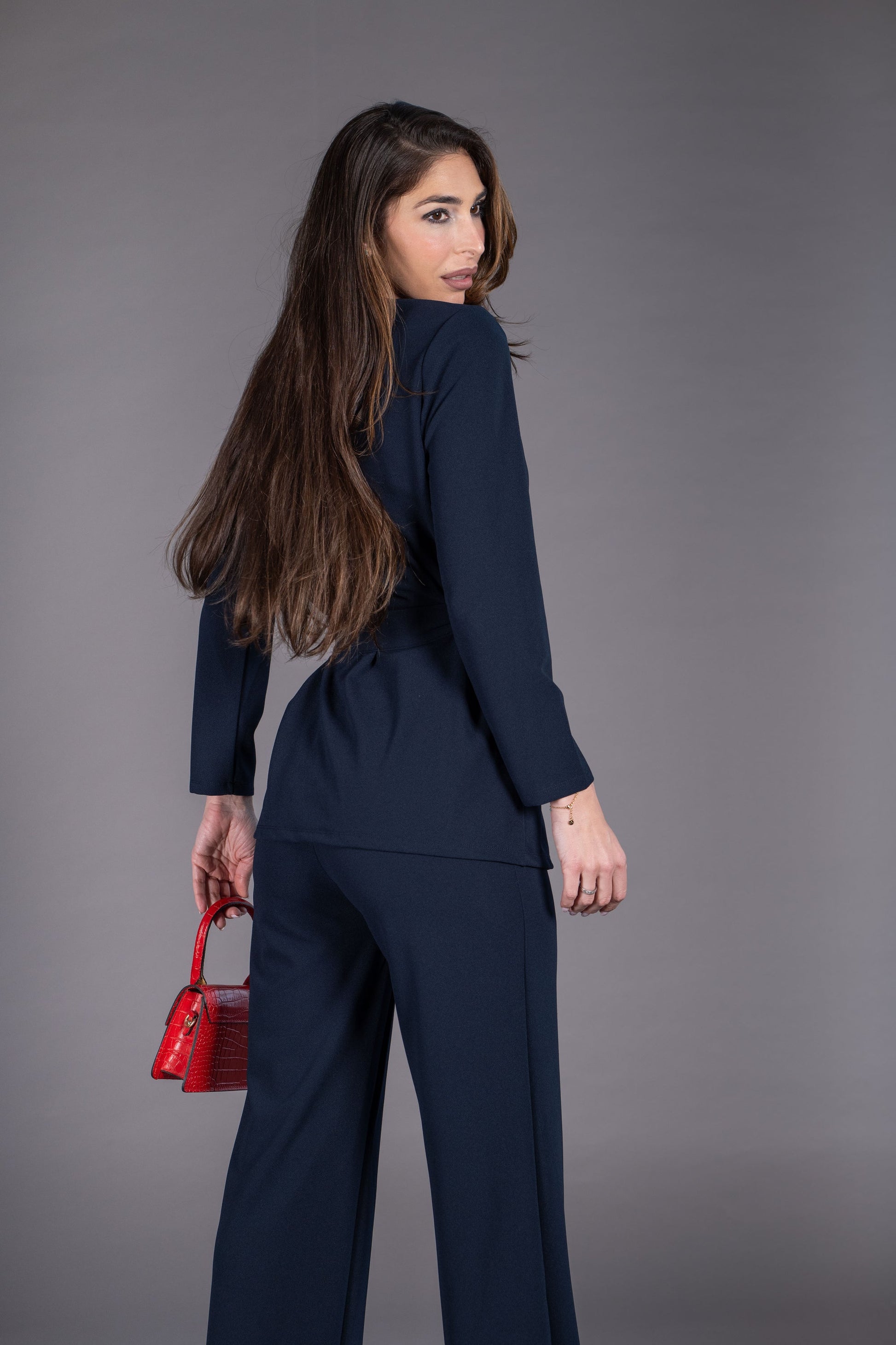 Woman in a navy suit holding a red handbag against a gray background