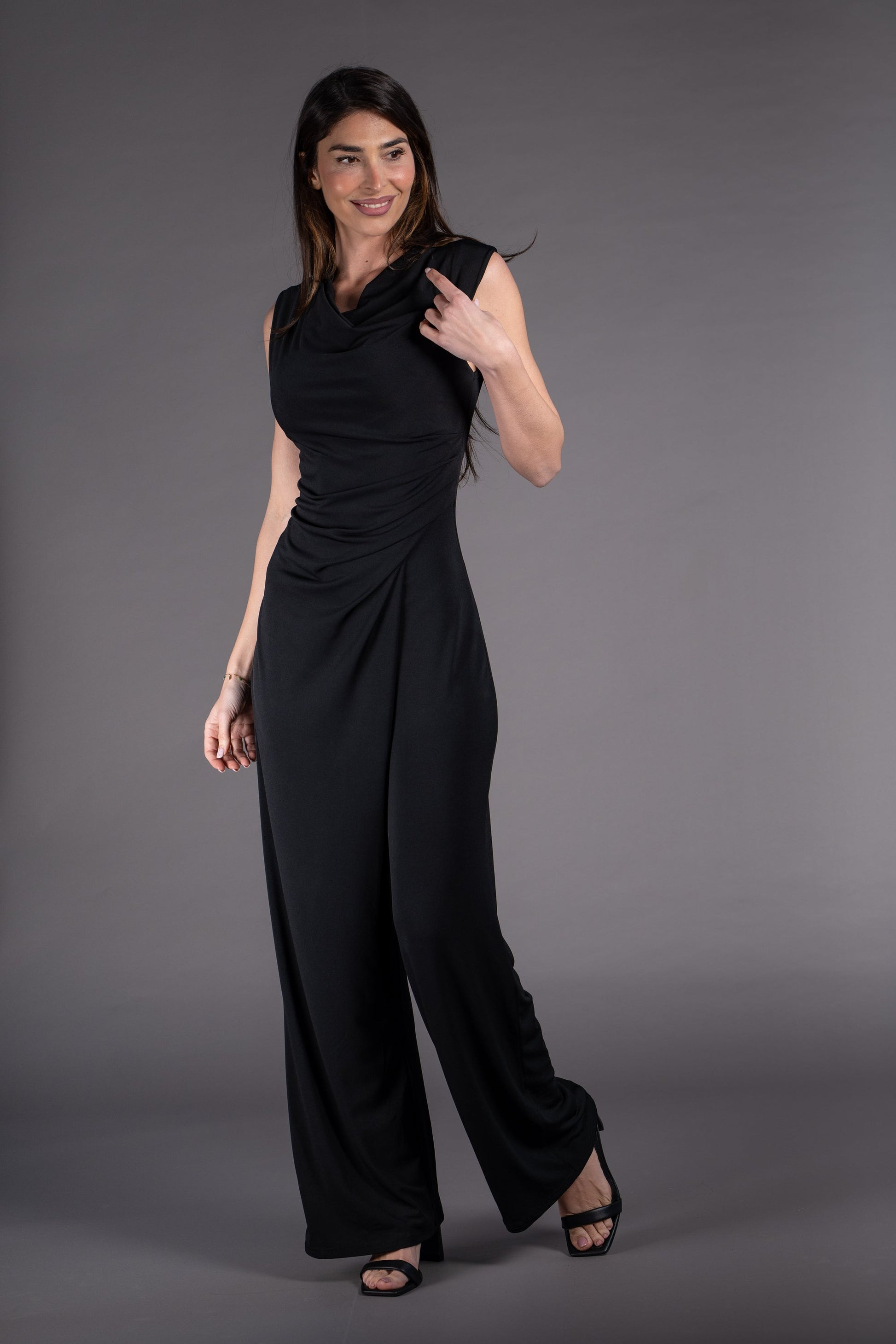 Woman wearing a black sleeveless jumpsuit against a gray background