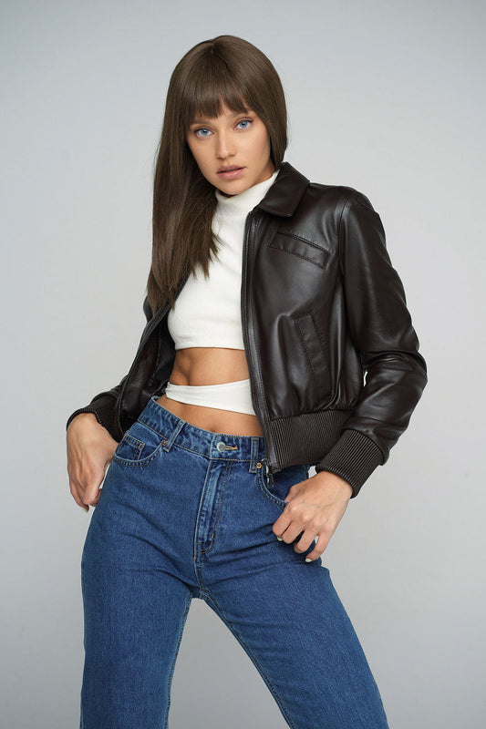 Woman wearing a brown leather jacket and blue jeans on a gray background