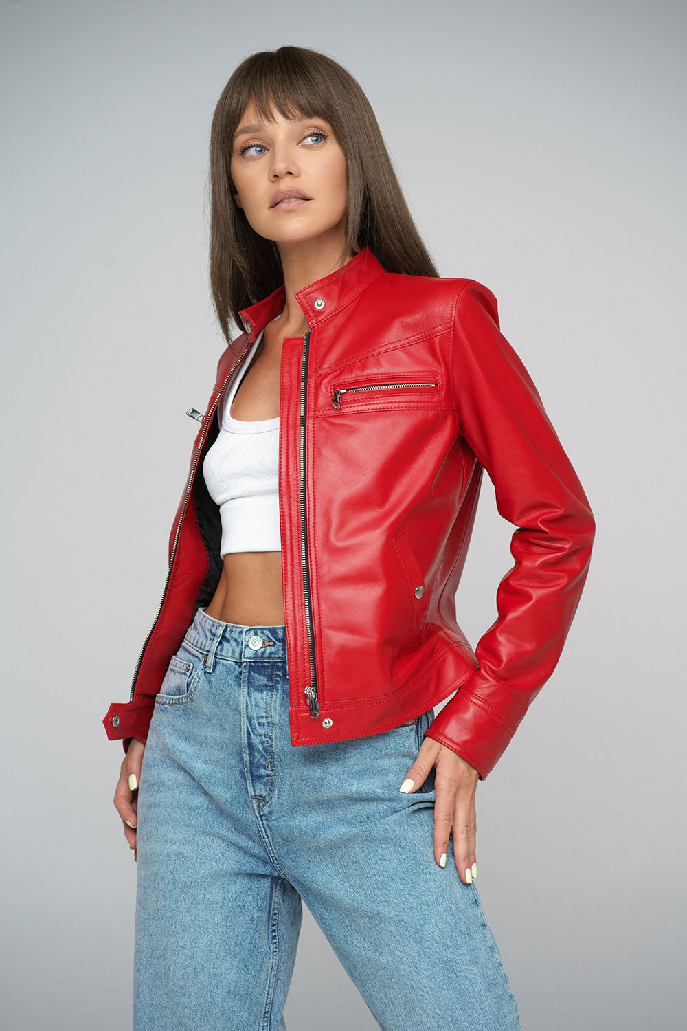 Woman wearing a red leather jacket and blue jeans on a gray background