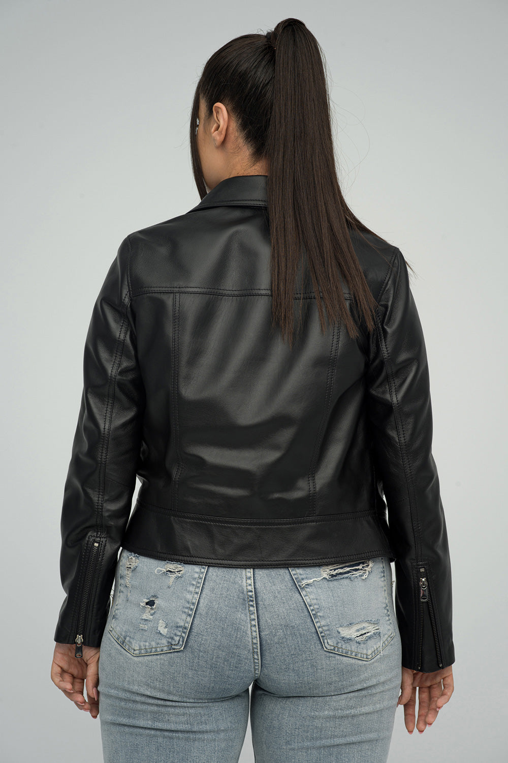 Person wearing a black leather jacket and light blue jeans on a gray background
